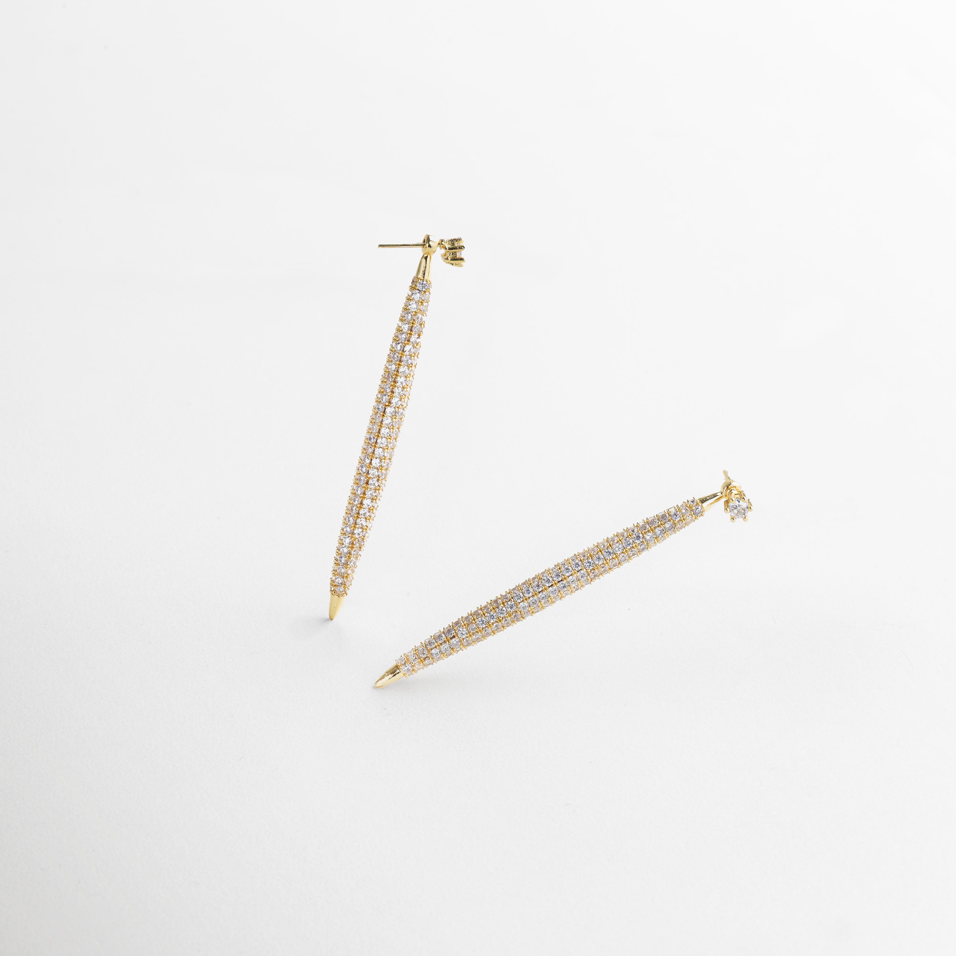 Aretes Tiznit dorados vistos de frente, con diseño alargado de 6 cm e incrustaciones brillantes de zirconias. Vista frontal de los aretes elegantes en chapa de oro 18K, con detalles que capturan la luz. Aretes largos dorados con zirconias vistos desde el frente, ideales para eventos formales o de noche. Primer plano de los Aretes Tiznit dorados, con forma estilizada y brillo deslumbrante. Par de aretes dorados alargados con incrustaciones de zirconia, perfectos para un look sofisticado.