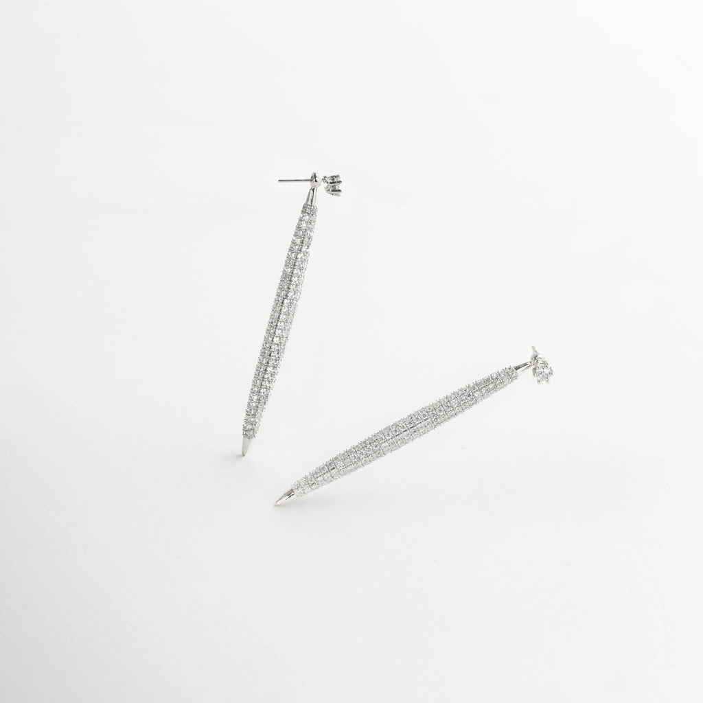 aretes plateados vista diagonal, detalle textura aretes, joyería plateada moderna, aretes brillantes largos, accesorios elegantes mujer, aretes con diseño estilizado, joyería contemporánea plateada, aretes refinados