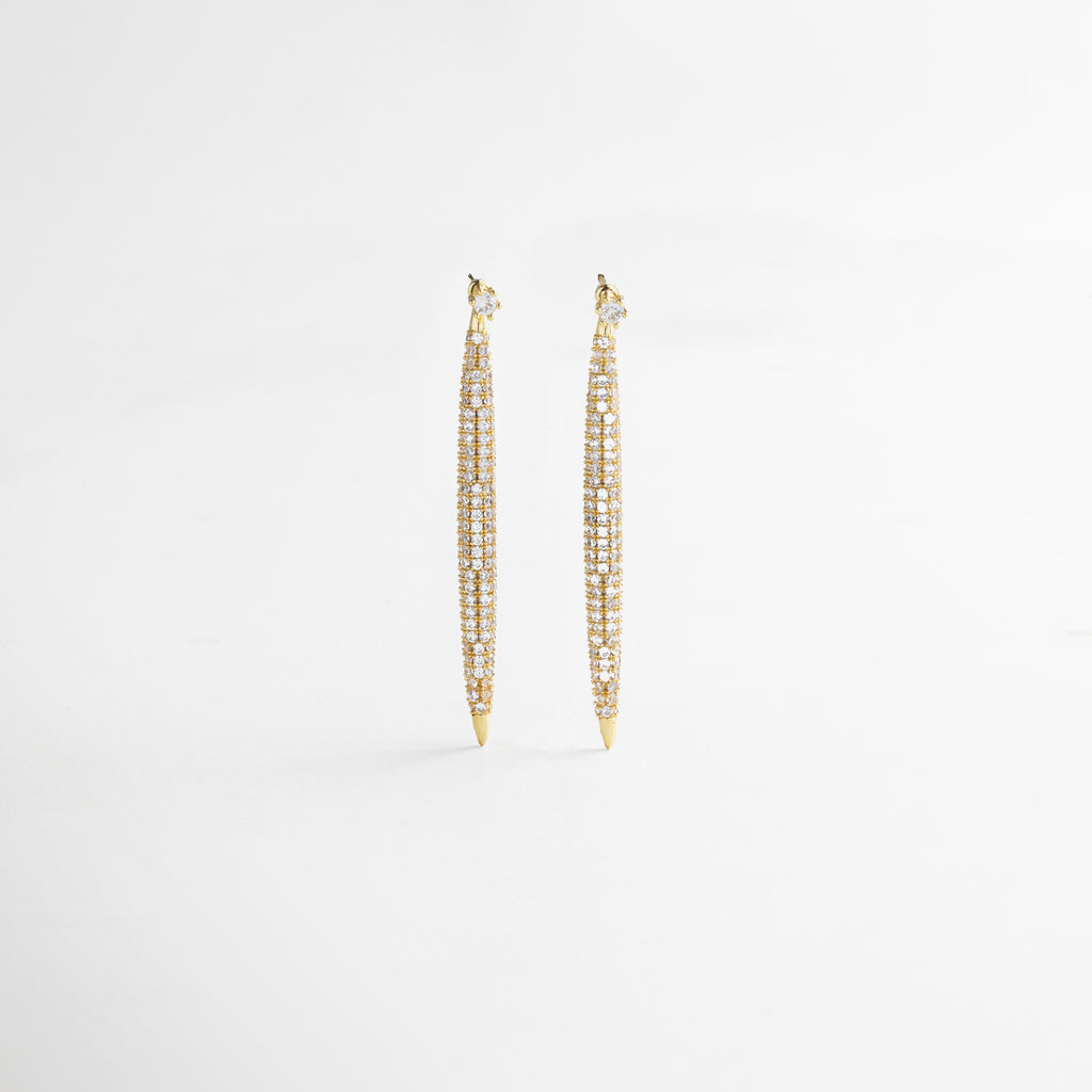 Vista lateral de los Aretes Tiznit dorados, mostrando su perfil delgado y la caída elegante del diseño. Aretes dorados vistos de lado, con forma estilizada que acompaña el movimiento con brillo y sutileza. Detalle lateral de arete largo con zirconias, ideal para ocasiones formales y looks refinados. Arete dorado de 6 cm visto de perfil, con diseño alargado y acabado lujoso. Aretes Tiznit en dorado desde el lateral, con brillo elegante y presencia sofisticada.