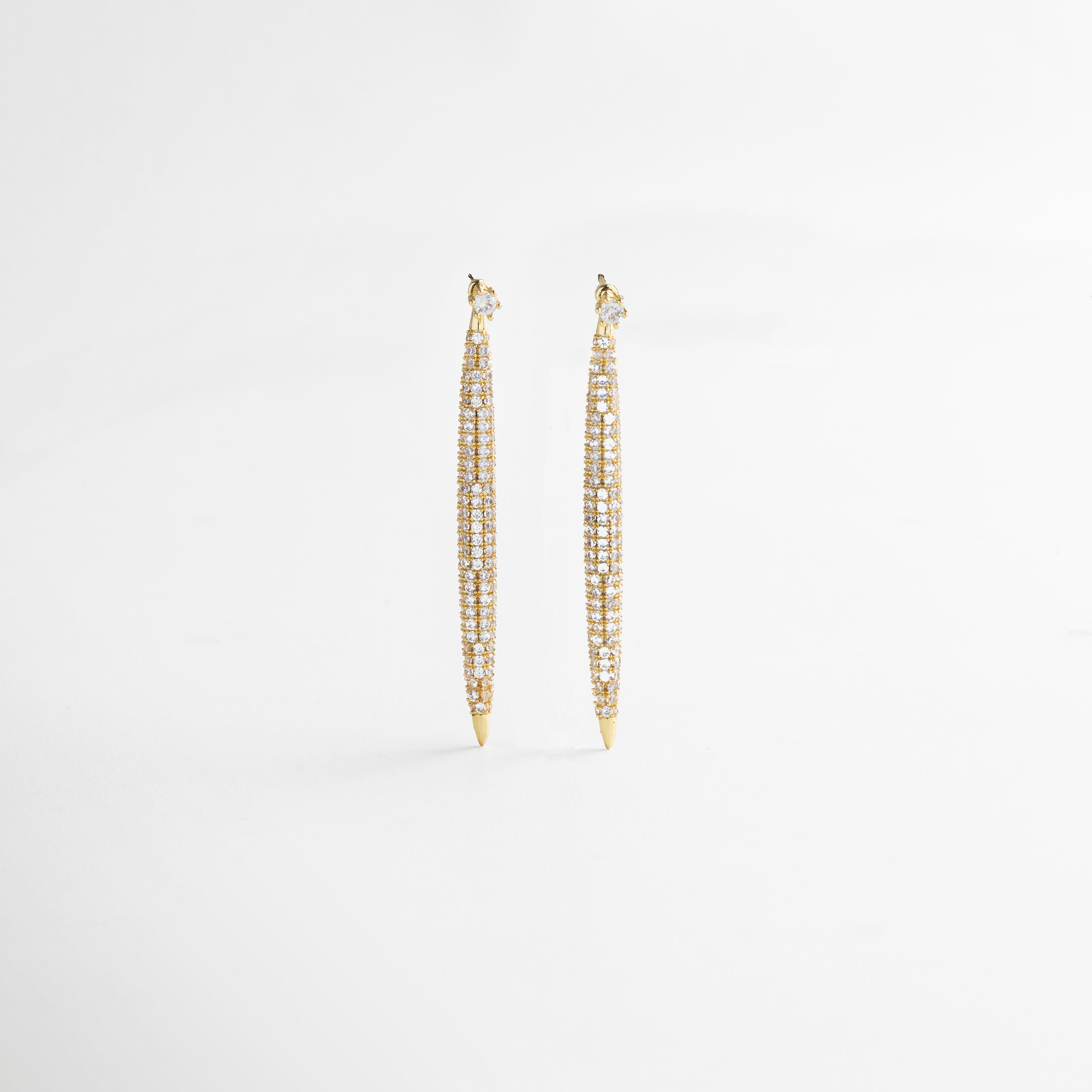 Vista lateral de los Aretes Tiznit dorados, mostrando su perfil delgado y la caída elegante del diseño. Aretes dorados vistos de lado, con forma estilizada que acompaña el movimiento con brillo y sutileza. Detalle lateral de arete largo con zirconias, ideal para ocasiones formales y looks refinados. Arete dorado de 6 cm visto de perfil, con diseño alargado y acabado lujoso. Aretes Tiznit en dorado desde el lateral, con brillo elegante y presencia sofisticada.