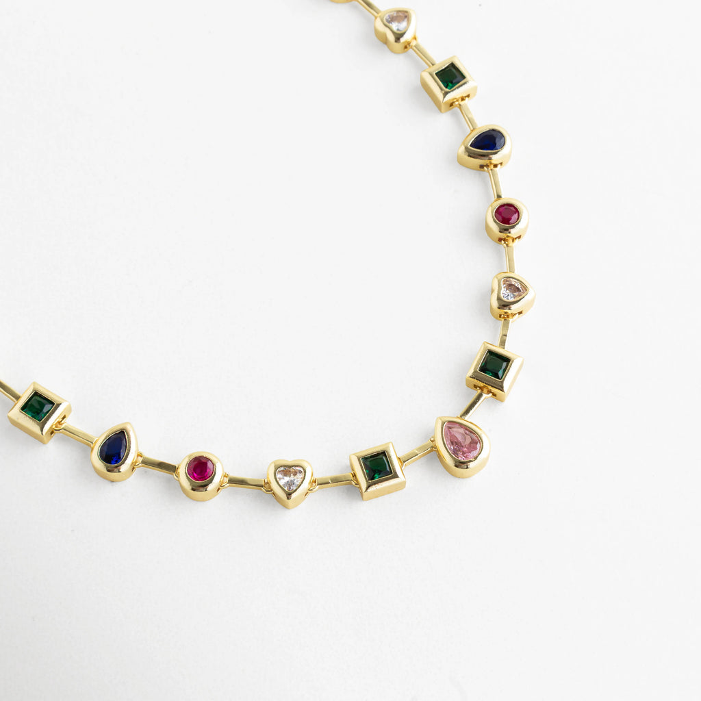 Collar dorado con piedras de colores en formas geométricas y acabado brillante, Detalle de collar con cristales multicolor en engaste dorado elegante, Collar fino con piedras verde, azul, rosa y rojo en diseño sofisticado, Primer plano de collar dorado con cristales sintéticos de colores vibrantes, Collar tipo cadena con incrustaciones de cristales multicolor y brillo pulido