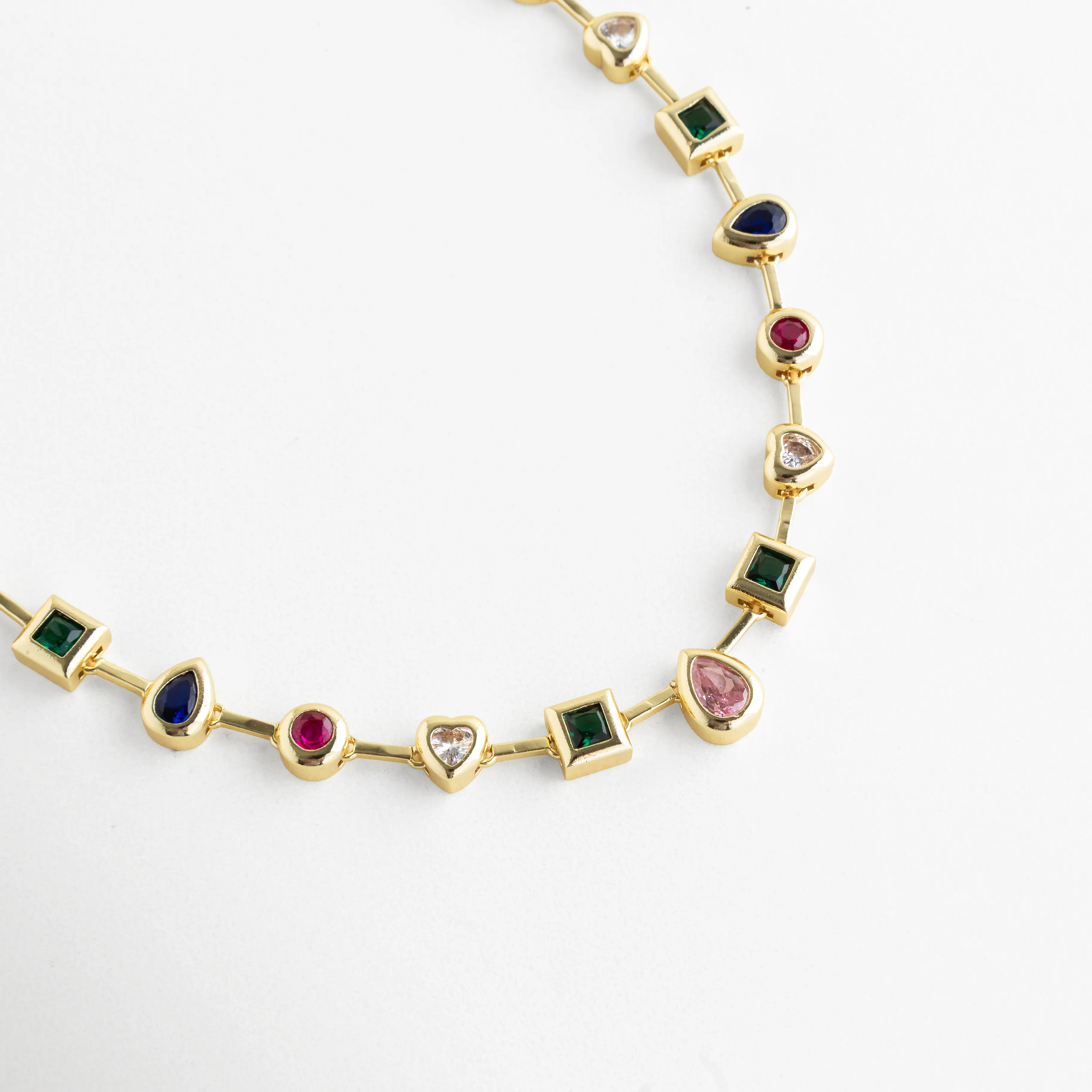 Collar dorado con piedras de colores en formas geométricas y acabado brillante, Detalle de collar con cristales multicolor en engaste dorado elegante, Collar fino con piedras verde, azul, rosa y rojo en diseño sofisticado, Primer plano de collar dorado con cristales sintéticos de colores vibrantes, Collar tipo cadena con incrustaciones de cristales multicolor y brillo pulido