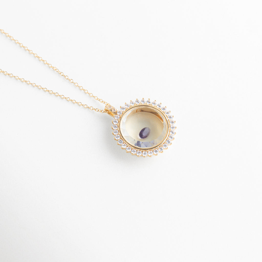Collar dorado con dije circular y piedra de cristal morada central, Dije elegante con cristal púrpura brillante en diseño delicado, Joyería fina con piedra violeta en accesorio minimalista, Collar delicado con cristal morado pequeño y brillante, Accesorio de bisutería con gema morada en diseño moderno