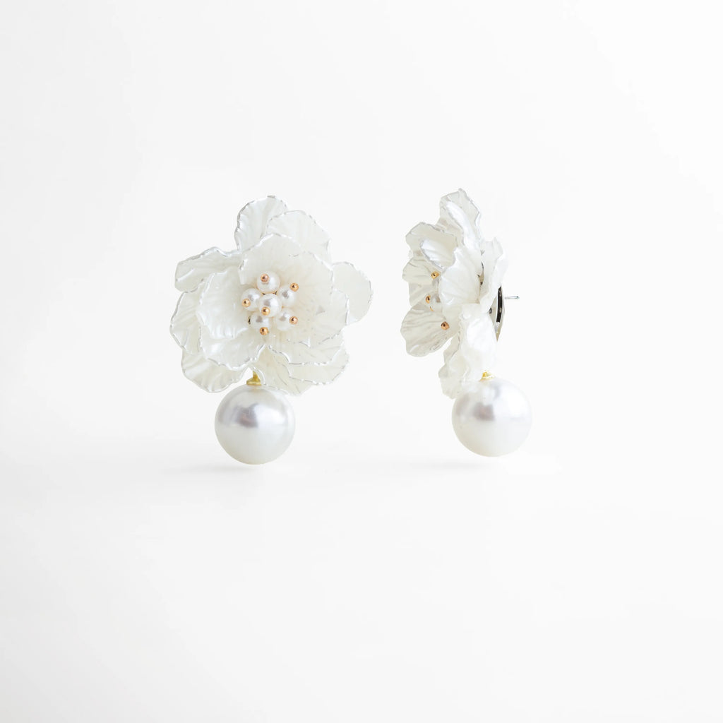 Aretes con flor tridimensional blanca y perla colgante elegante, Vista lateral de aretes Pearl Bloom con pétalos texturizados y perla, Aretes florales con volumen y perla decorativa en acabado refinado, Detalle de aretes con diseño floral y perla colgante brillante, Aretes largos con estructura ligera y flor blanca elegante
