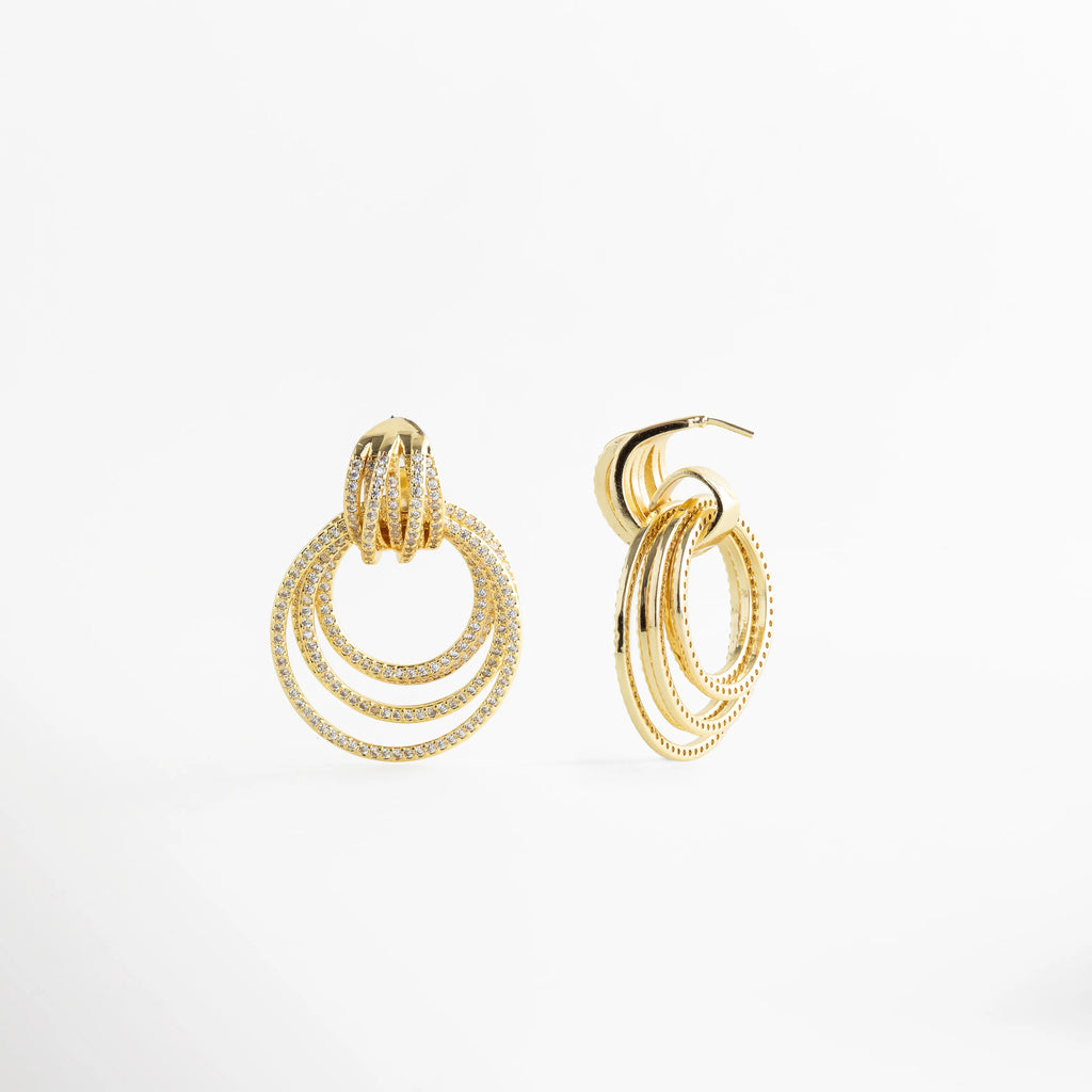 Aretes Elarisse dorados con zirconias en detalle, diseño de aros brillantes, Detalle de Aretes Elarisse con zirconias y acabado en oro 18K luminoso, Aretes Elarisse con diseño circular en capas y zirconias en vista cercana, Aretes Elarisse elegantes con brillo intenso y textura en zirconias, Primer plano de Aretes Elarisse dorados con diseño glam y zirconias