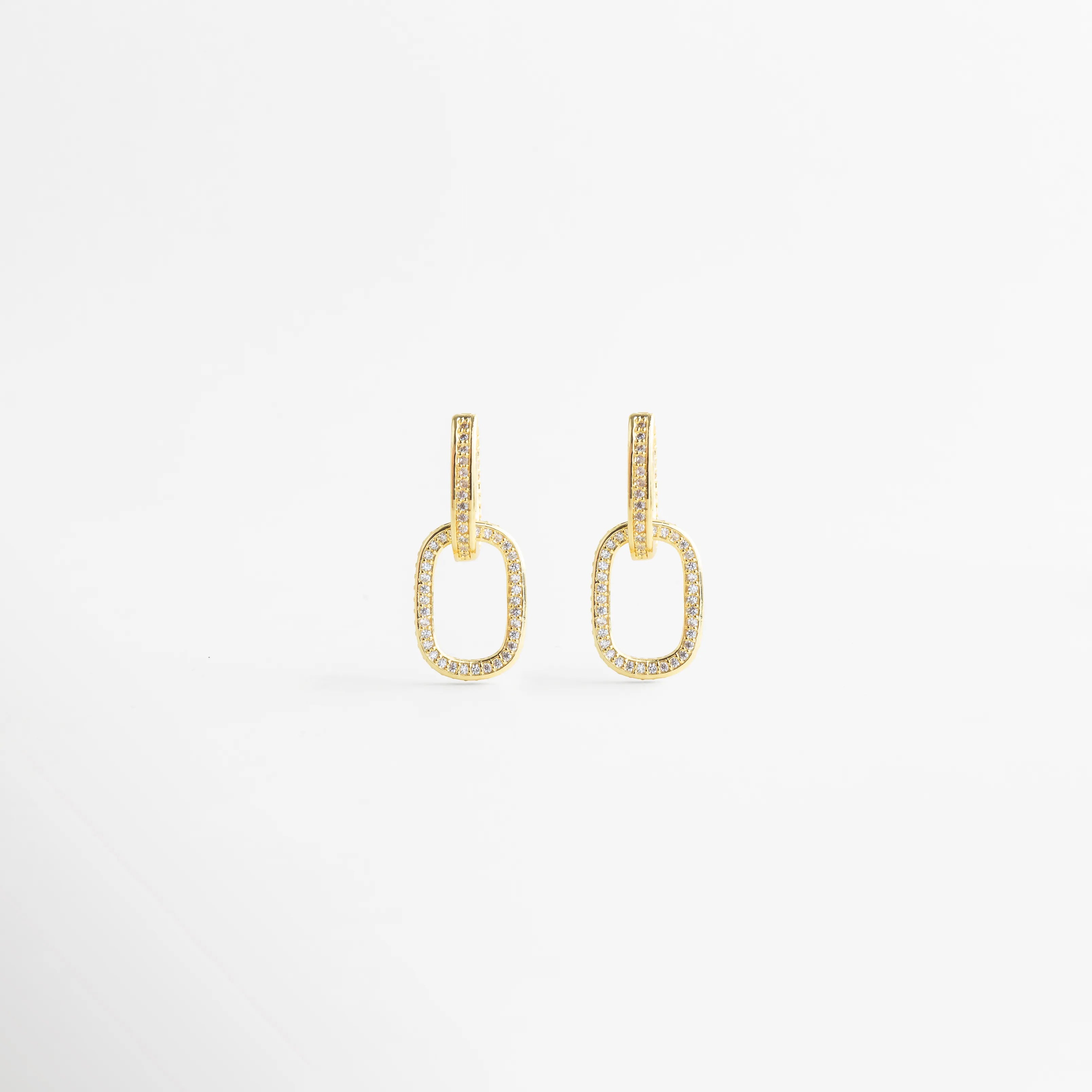 Pendientes de aro dorados con diseño de eslabón ovalado y circonitas incrustadas, Arracadas de oro con pavé de cristales brillantes en forma de eslabón doble, Aretes colgantes dorados elegantes con detalles de piedras brillantes sobre fondo blanco, Pendientes de eslabón bañados en oro con microcirconitas para look de fiesta, Joyería fina: pendientes ovalados de oro con cristales pequeños estilo minimalista.
