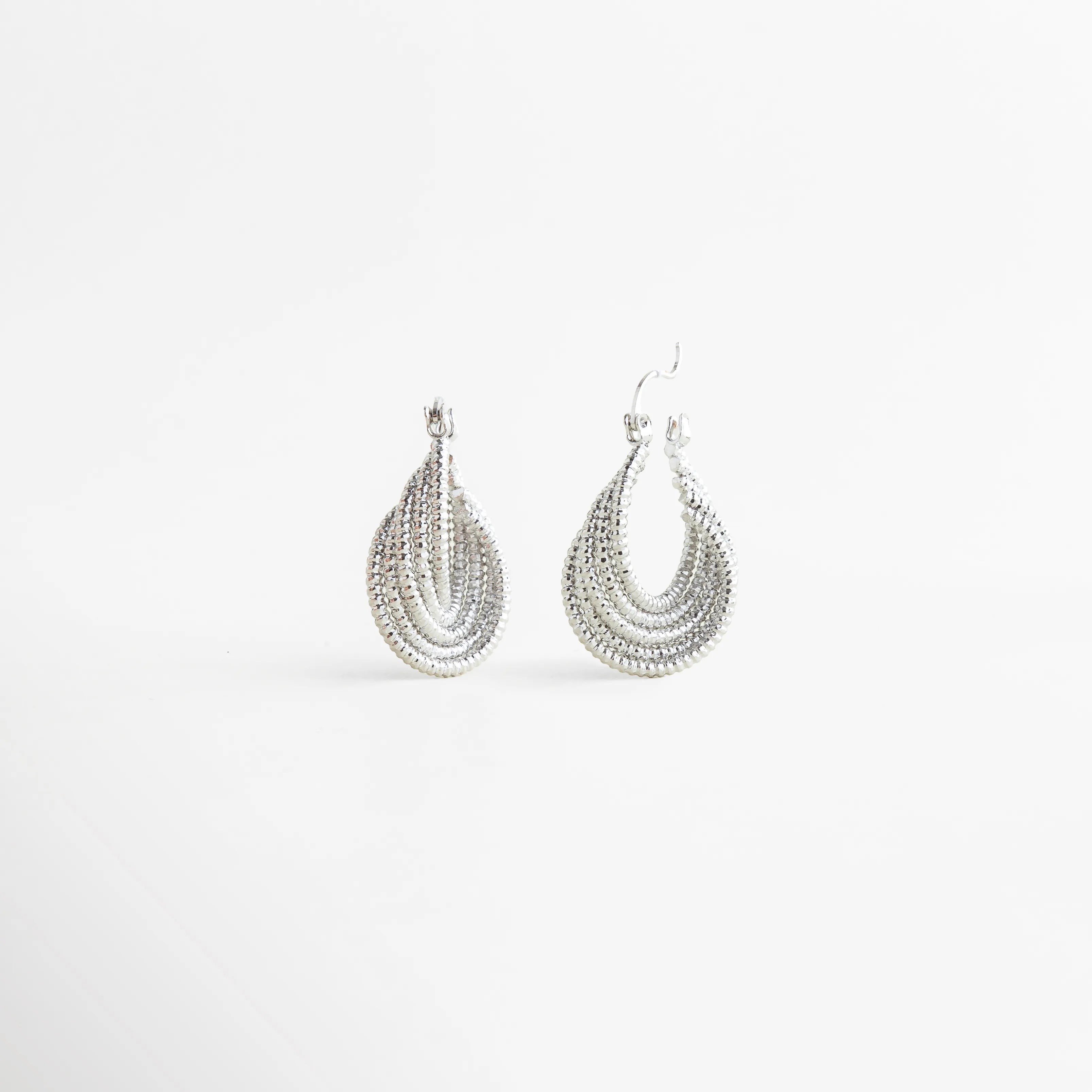 Aretes Amarielle plateados en detalle con diseño geométrico y acabado brillante, Detalle de Aretes Amarielle con textura en capas y brillo elegante, Aretes Amarielle con forma ovalada y acabado luminoso en vista cercana, Aretes Amarielle elegantes con diseño moderno y estructura en capas, Primer plano de Aretes Amarielle plateados con estilo minimalista sofisticado