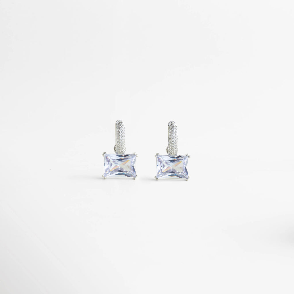 Aretes Clarisse Hoops en oro blanco con zirconia cuadrada brillante, diseño elegante y femenino, Par de aretes pequeños Clarisse Hoops con incrustación de zirconia y acabado enchapado en oro blanco, Aretes de cobre con recubrimiento en oro blanco y zirconia, estilo refinado para uso diario o eventos, Vista frontal de aretes Clarisse Hoops con piedra zirconia cuadrada y acabado brillante en tono plata, Aretes elegantes de zirconia Clarisse Hoops con diseño delicado y sofisticado en oro blanco.