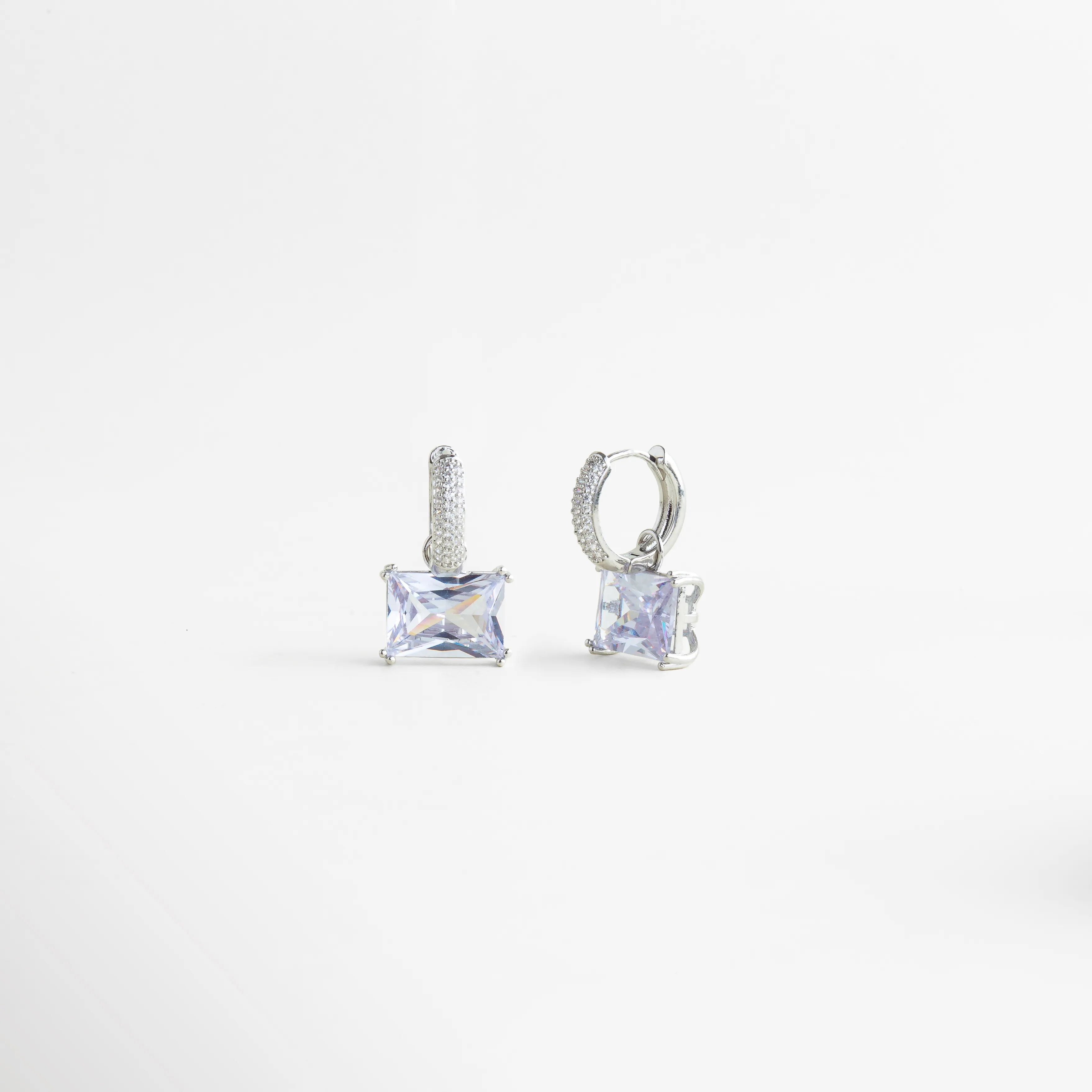 Aretes Clarisse Hoops vistos en ángulo, con zirconia brillante y estructura delicada en oro blanco, Vista lateral de aretes pequeños con zirconia cuadrada y acabado enchapado en oro blanco, Aretes de mujer Clarisse Hoops con diseño fino y elegante, mostrados en perspectiva, Par de aretes con zirconia transparente y detalle metálico en cobre recubierto de oro blanco, Aretes sofisticados Clarisse Hoops con brillo sutil y diseño femenino en vista diagonal.