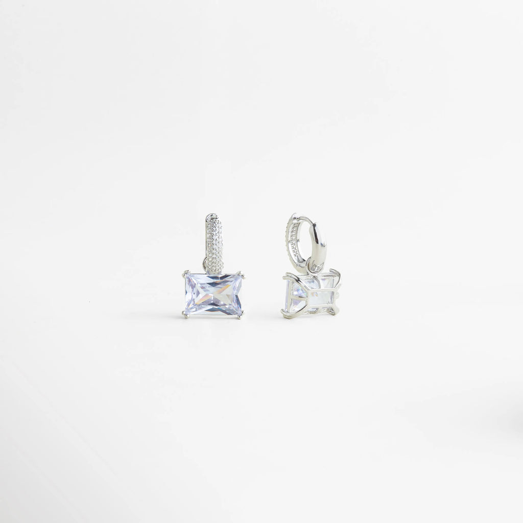 Aretes Clarisse Hoops en vista lateral mostrando su estructura tipo hoop con zirconia engastada, Detalle de aretes pequeños de zirconia con acabado en oro blanco y diseño elegante de aro, Vista de perfil de aretes Clarisse Hoops con piedra brillante y silueta delicada, Aretes de cobre enchapados en oro blanco con zirconia, diseño refinado y femenino, Detalle lateral de aretes hoop pequeños con zirconia cuadrada y acabado brillante.
