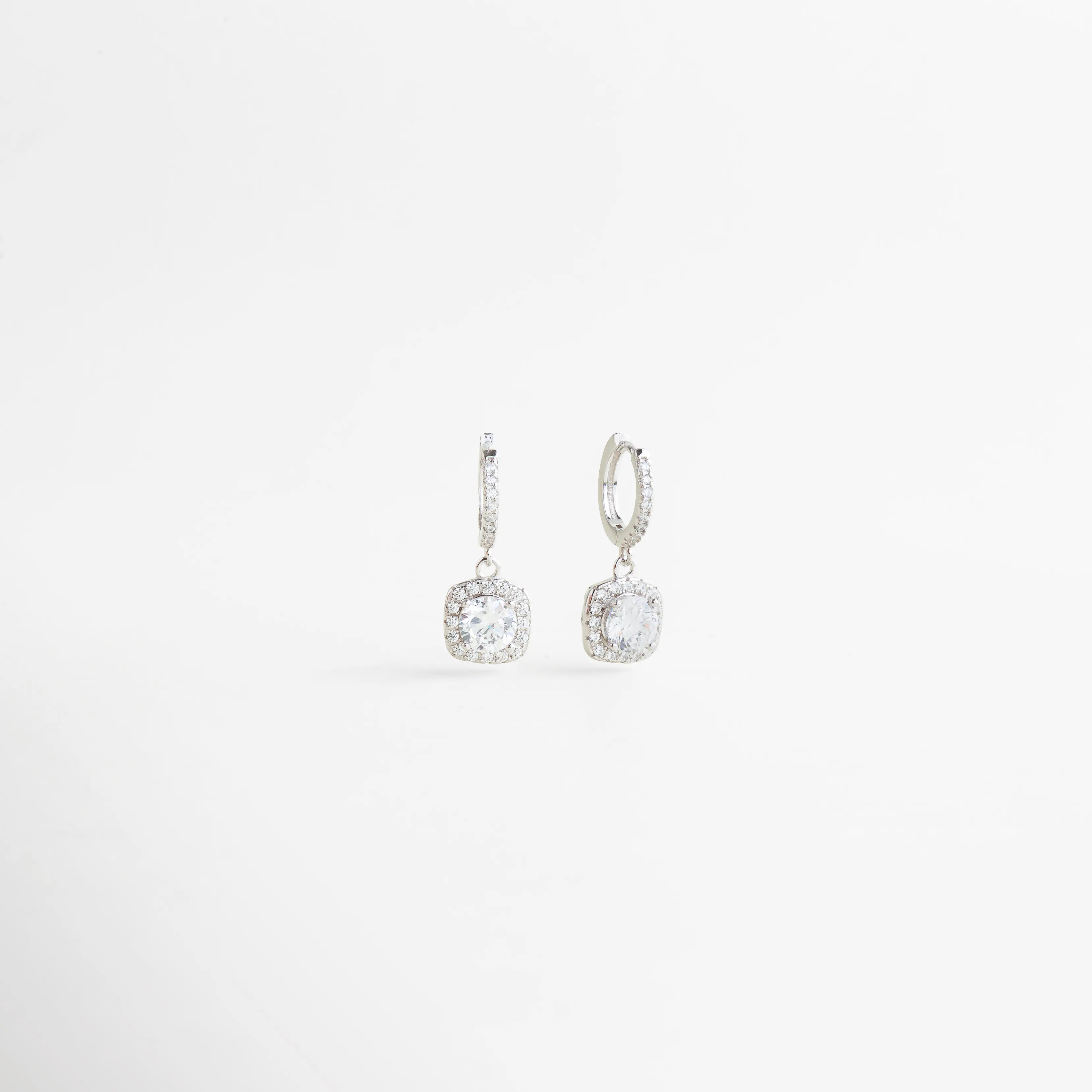 Aretes de zirconia en vista diagonal con diseño colgante y acabado elegante en plata, Vista lateral de aretes femeninos con aro pequeño y zirconia brillante colgante, Aretes delicados de Plata Ley 925 mostrados en ángulo para destacar su brillo y forma, Diseño sofisticado de aretes colgantes con zirconia redonda y acabado refinado, Aretes elegantes para mujer con caída sutil y piedra brillante en vista diagonal.