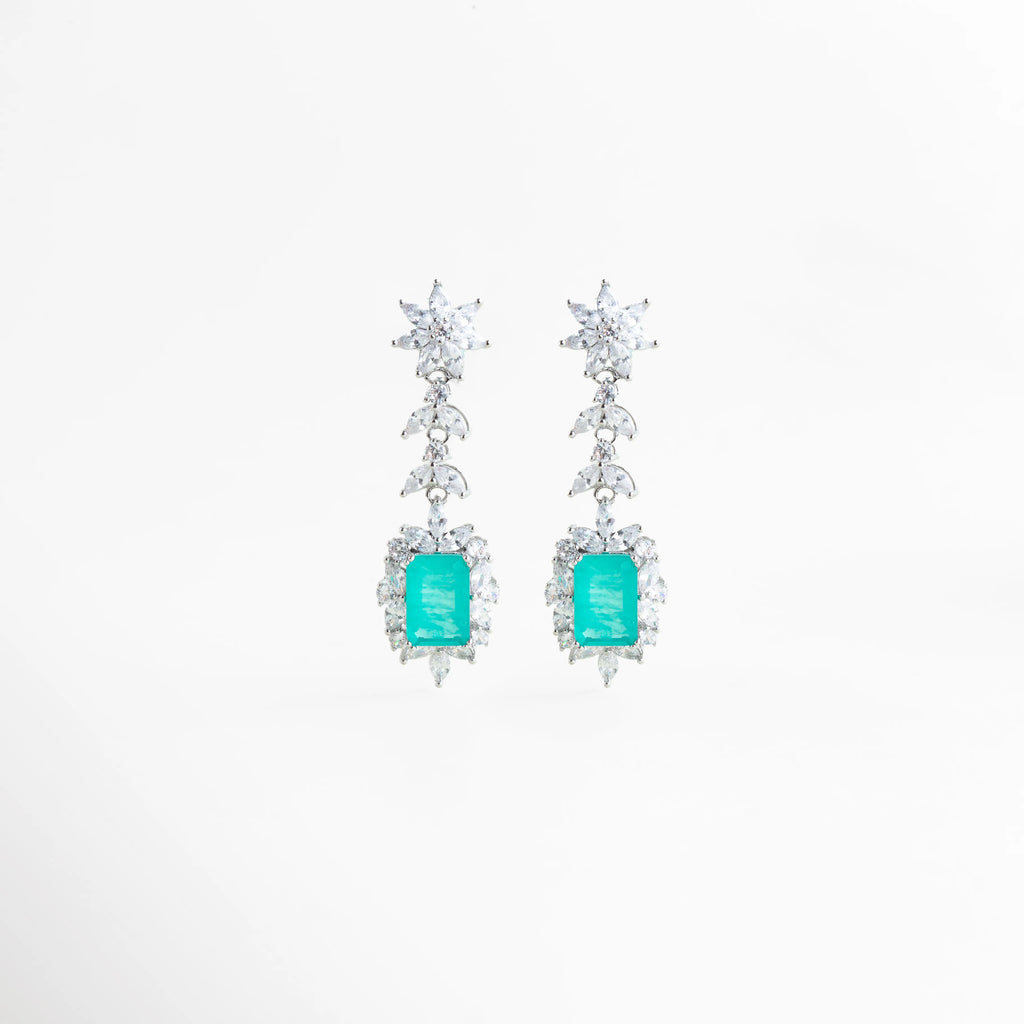 Aretes largos Cordelia en acabado de plata de rodio con gema central color turquesa y halo de circonias brillantes, Pendientes de gala con piedra rectangular aguamarina y diseño de hojas de cristal en cascada, Vista frontal de aretes elegantes de 5 cm de largo con circonias blancas y centro color turquesa intenso, Joyería de lujo: aretes con recubrimiento de rodio y piedras preciosas de laboratorio en tono aguamarina, Par de aretes Cordelia Turquesa resaltando el corte esmeralda de la gema central y el 