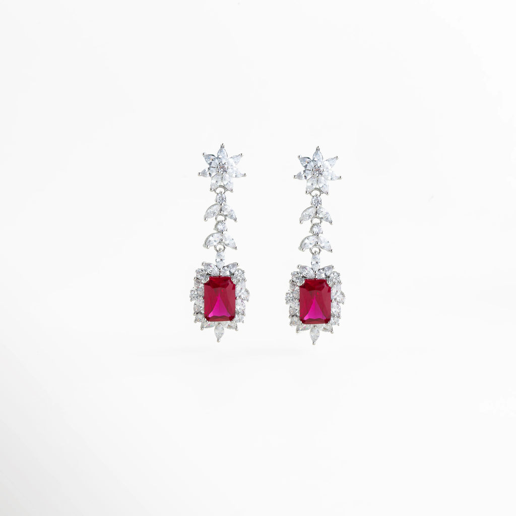 Aretes largos en acabado de plata de rodio con gema central roja y halo de circonias brillantes, Pendientes de gala con piedra roja rectangular y diseño de hojas de cristal en cascada, Vista frontal de aretes elegantes de 5 cm de largo con circonias blancas y centro color rubí, Joyería de lujo: aretes con recubrimiento de rodio y piedras preciosas de imitación en color rojo, Par de aretes Rojos resaltando el corte esmeralda de la gema central y el brillo del pavé.