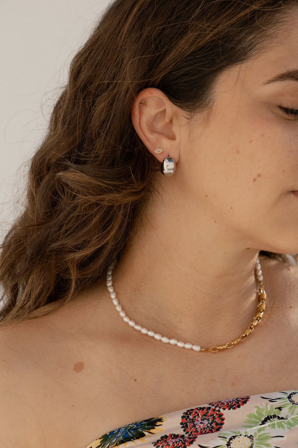 Mujer con collar de perlas blancas y cadena dorada de eslabones gruesos, Detalle de joyería mixta: gargantilla de perlas naturales y mitad de oro, Primer plano de modelo con collar de perlas, cadena dorada y arete pequeño, Diseño de joyería contemporánea con perlas blancas y eslabones de oro, Gargantilla bicolor de perlas y cadena metálica lucida por una modelo.