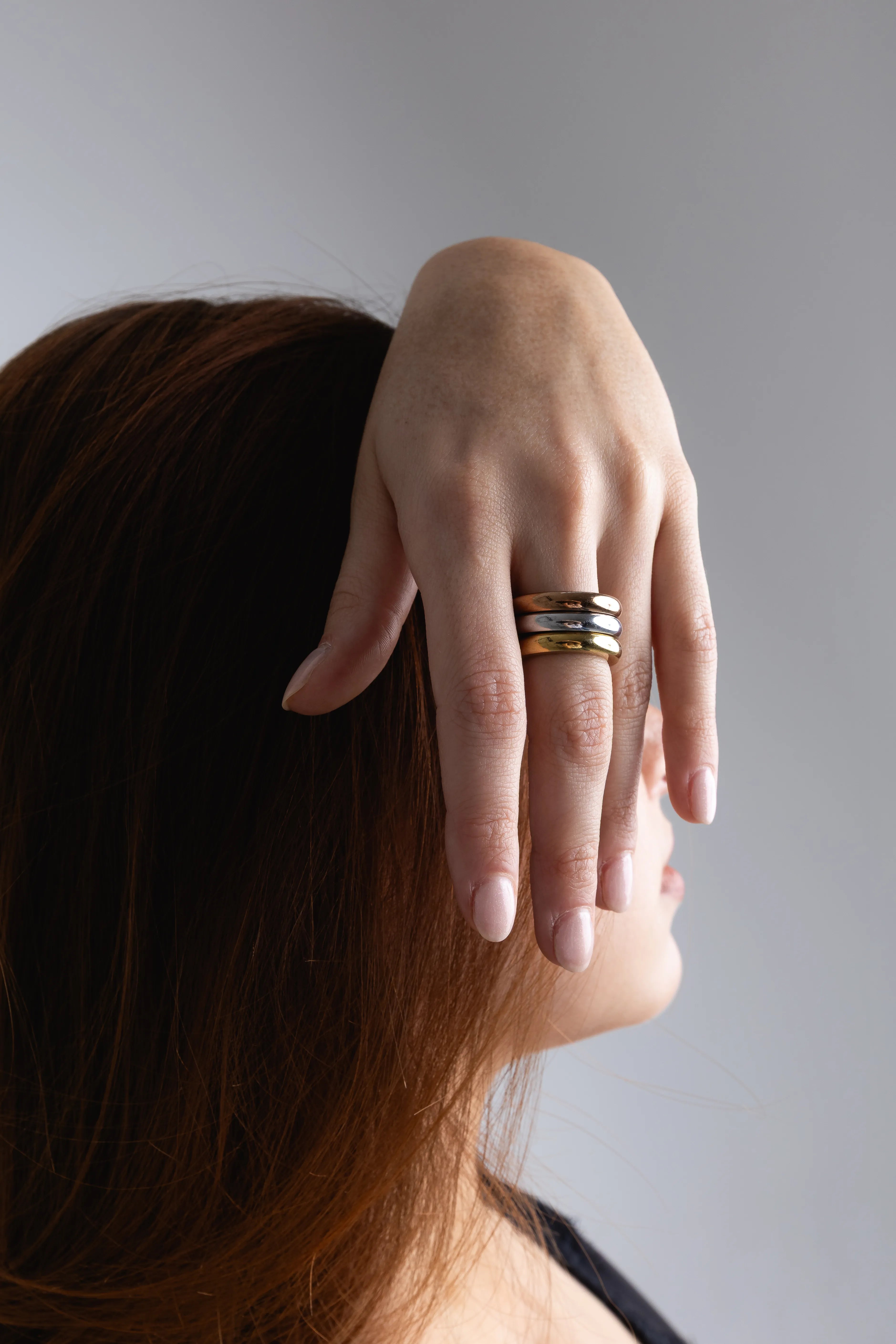 Modelo luciendo un set de anillos apilados en tonos oro, plata y oro rosa, Detalle de varios anillos finos de diferentes metales usados en un mismo dedo, Combinación de anillos minimalistas de colores mezclados en la mano de una mujer, Set de anillos apilables con diferentes acabados metálicos sobre fondo neutro, Primer plano de joyería moderna: anillos delgados en oro y plata combinados.