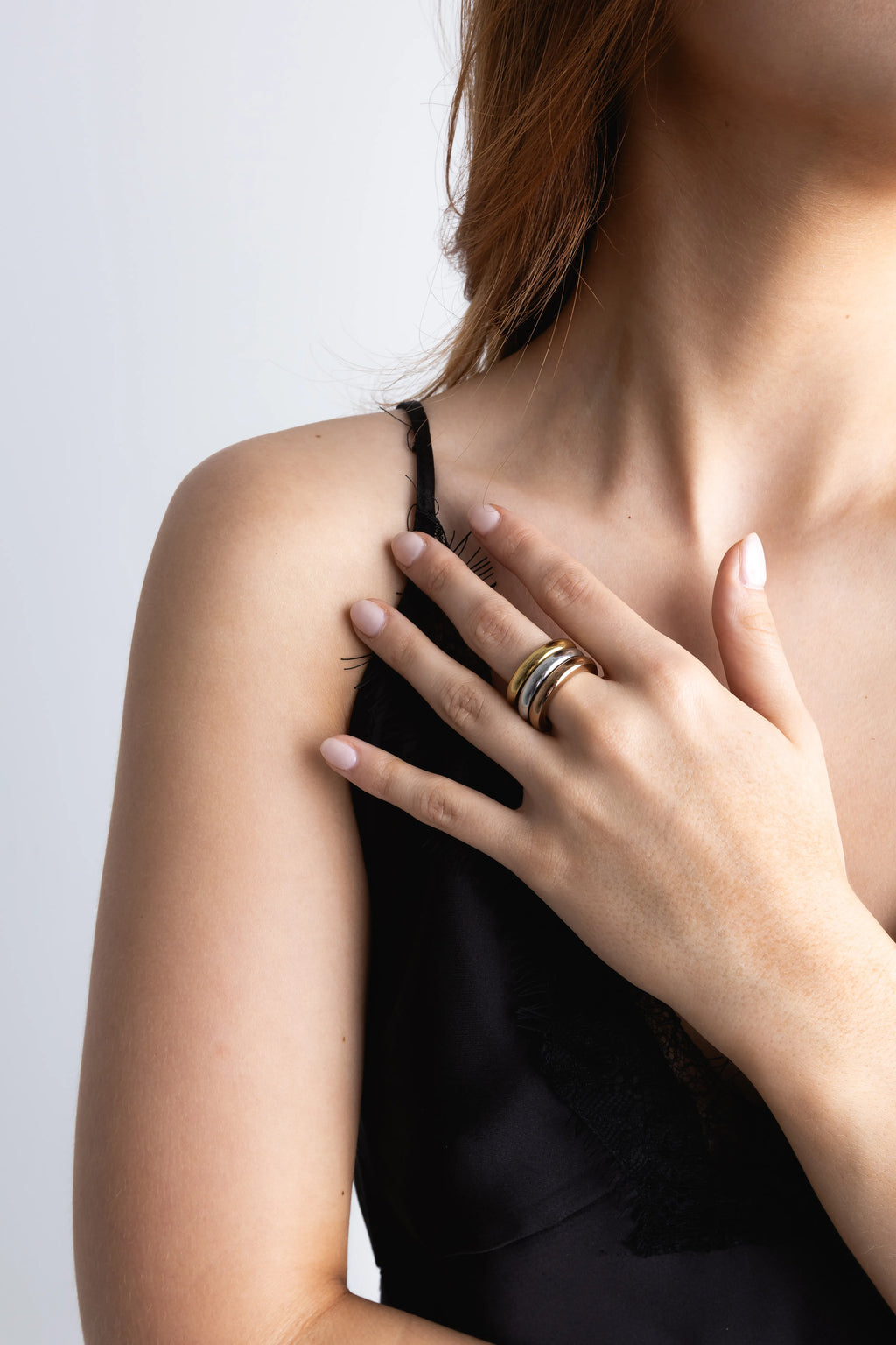 Modelo luciendo un set de tres anillos apilables de metal mixto (oro y plata) en el dedo índice, Detalle de un anillo tricolor apilable con diseño abombado y texturizado en la mano de una mujer, Combinación de tres anillos minimalistas en oro, plata y oro rosa en una sola pieza de joyería, Set de anillos apilables con diferentes acabados metálicos en la mano de una modelo con top de encaje, Primer plano de joyería moderna: un anillo grueso y tricolor sobre el hombro de una mujer.