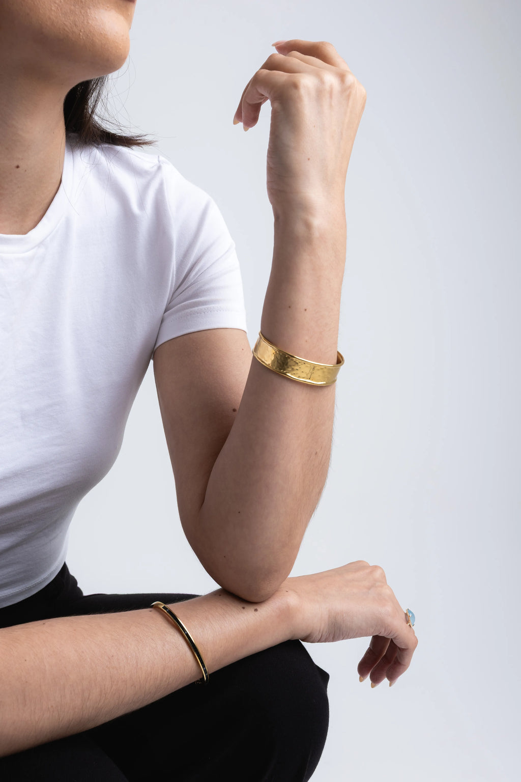Mujer usando pulsera dorada elegante con diseño moderno en primer plano, Detalle de pulsera dorada en muñeca combinada con look casual blanco, Pulsera dorada brillante en uso con outfit minimalista femenino, Close-up de accesorio dorado en muñeca con estilo sofisticado y moderno, Mujer con pulsera dorada ajustada, look casual elegante y contemporáneo