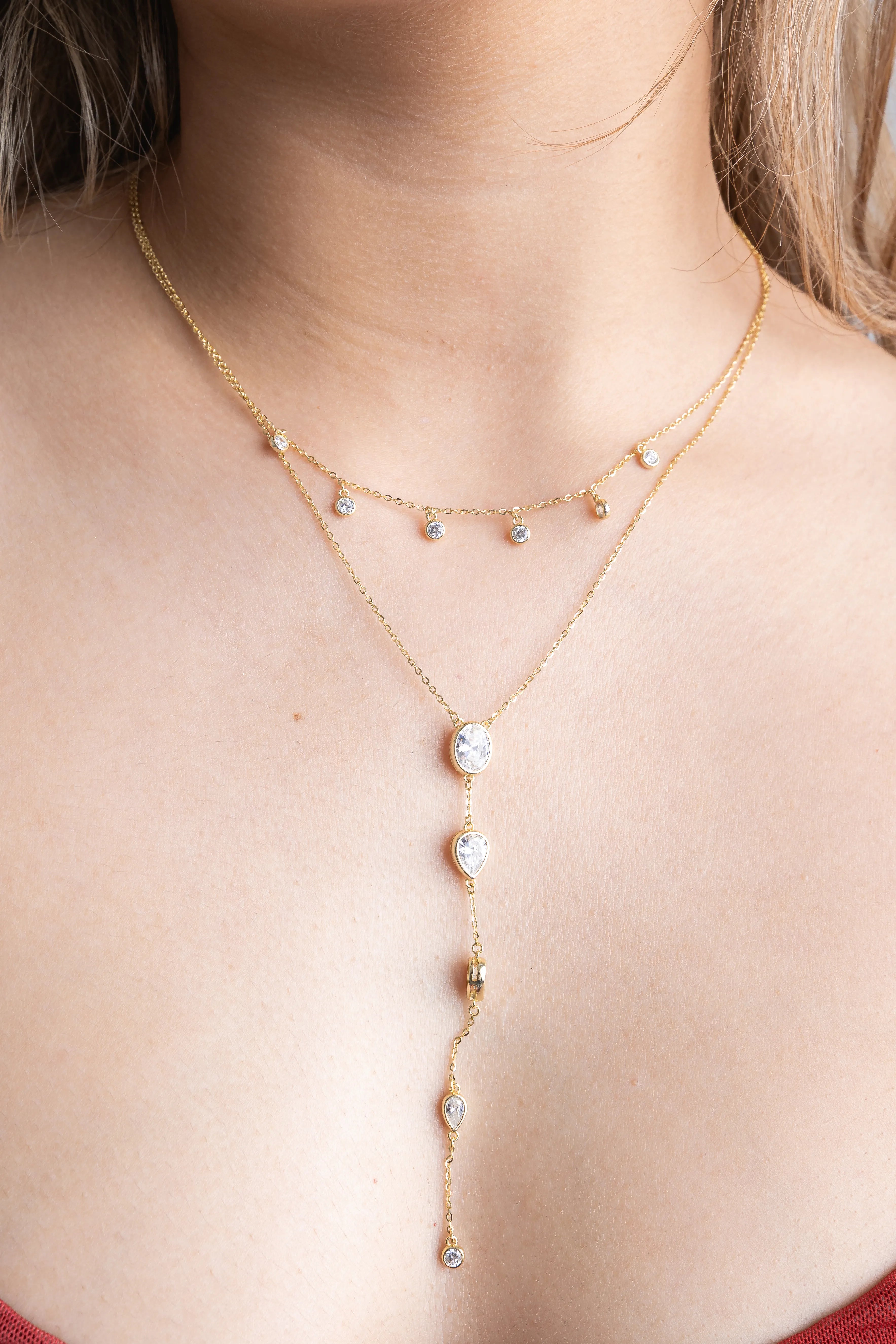 Collar de doble capa en oro con pequeños dijes de cristal brillantes y caída estilo corbata, Gargantilla doble dorada con detalles de circonias circulares y colgantes en forma de gota, Joyería fina: collar lariat de oro con múltiples piedras blancas brillantes sobre la piel, Doble cadena de oro con cristales colgantes y diseño de cascada central, Primer plano de collar dorado multinivel con brillantes transparentes y acabado minimalista.