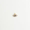 Dije mini de ojo turco dorado con pavé de zirconias transparentes y piedra azul central, Charm de cobre enchapado en oro en forma de ojo místico de Amalaya Jewelry, Dije protector de ojo turco de 1 cm para personalizar cadenas y pulseras de moda, Amuleto de joyería dorado con zirconia azul zafiro sobre fondo blanco texturizado, Charm para armar joyería con silueta de ojo místico de la suerte y cristales.