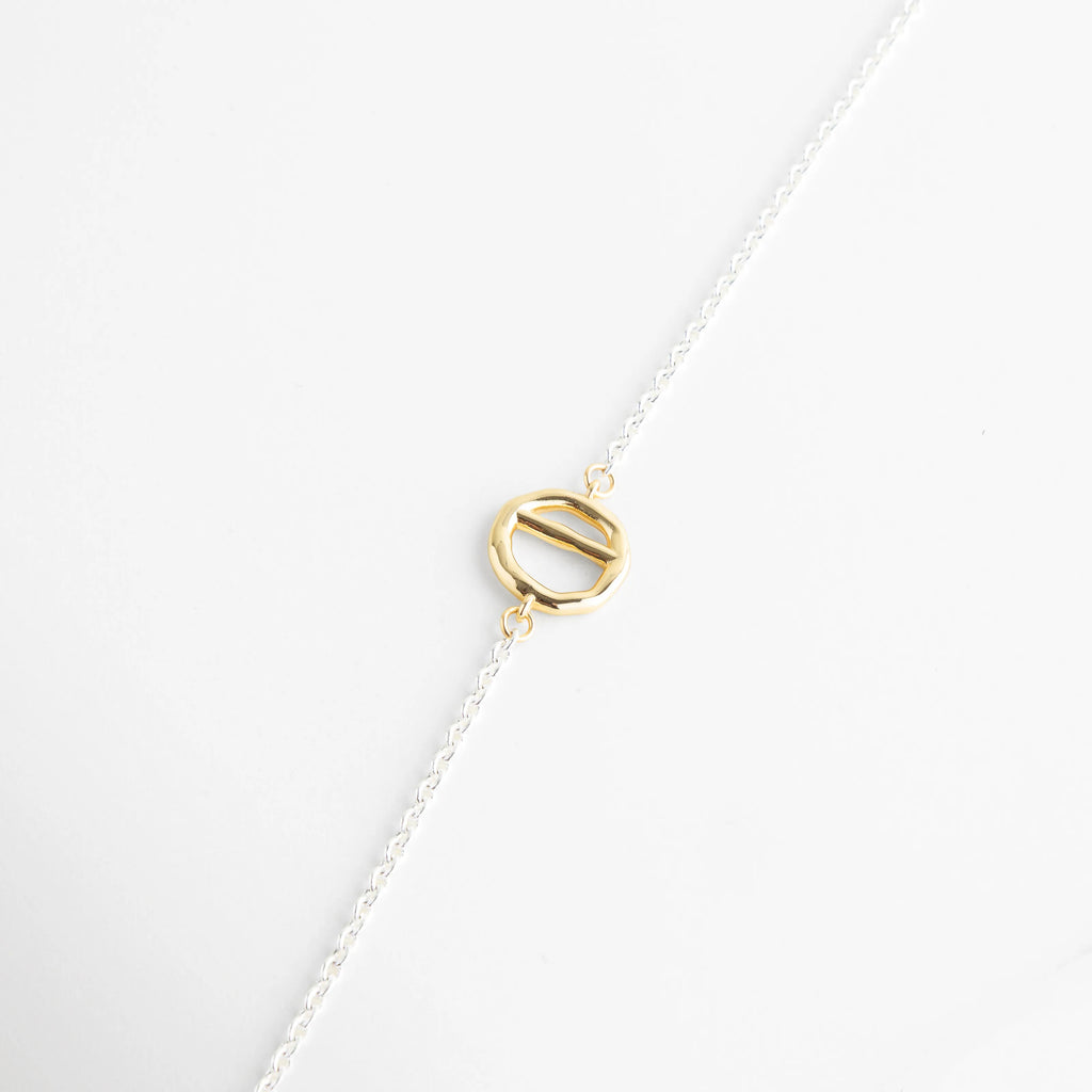 Composición de las piezas del collar: cierre T-Bar, placa circular y cadena platinada, Muestra de los elementos dorados de 18K que componen el collar bi-color de 37 cm, Vista detallada de los herrajes dorados sobre el fondo blanco de joyería fina, Separación visual de los dijes geométricos y la cadena de oro blanco 18K, Detalle de los acabados mixtos en collar de cobre con recubrimiento de lujo.
