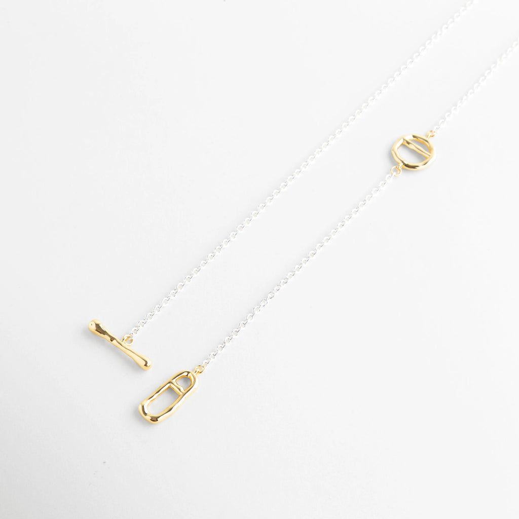 Collar tipo lariat con caída elegante mostrando el contraste de oro 18K y platinado, Vista diagonal de collar de 37 cm con detalles dorados y cadena de oro blanco, Diseño asimétrico de collar bi-tono con cierre T-Bar y elementos geométrico, Perspectiva de collar largo minimalista con acabados mixtos en oro y plata, Collar de cadena fina con caída ajustable y detalles enchapados en oro de 18K.