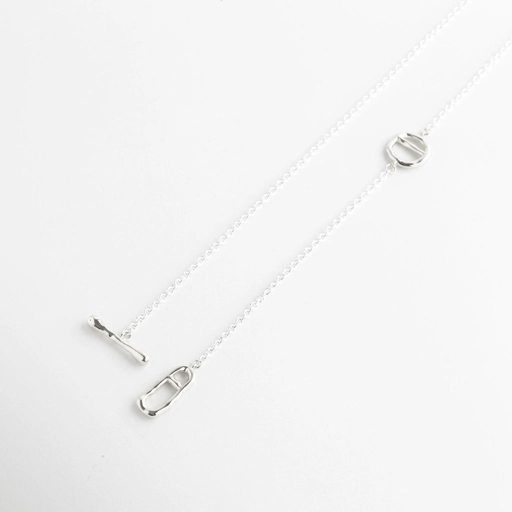 Muestra de la caída asimétrica de collar lariat en color plata brillante, Collar ajustable de oro blanco 18K con terminación de dije ovalado calado, Perspectiva lateral de collar minimalista resaltando el brillo del acabado platinado, Cadena de 37 cm con diseño de nodos geométricos en baño de oro blanco, Vista en ángulo de collar tipo corbatero con elementos de diseño contemporáneo.