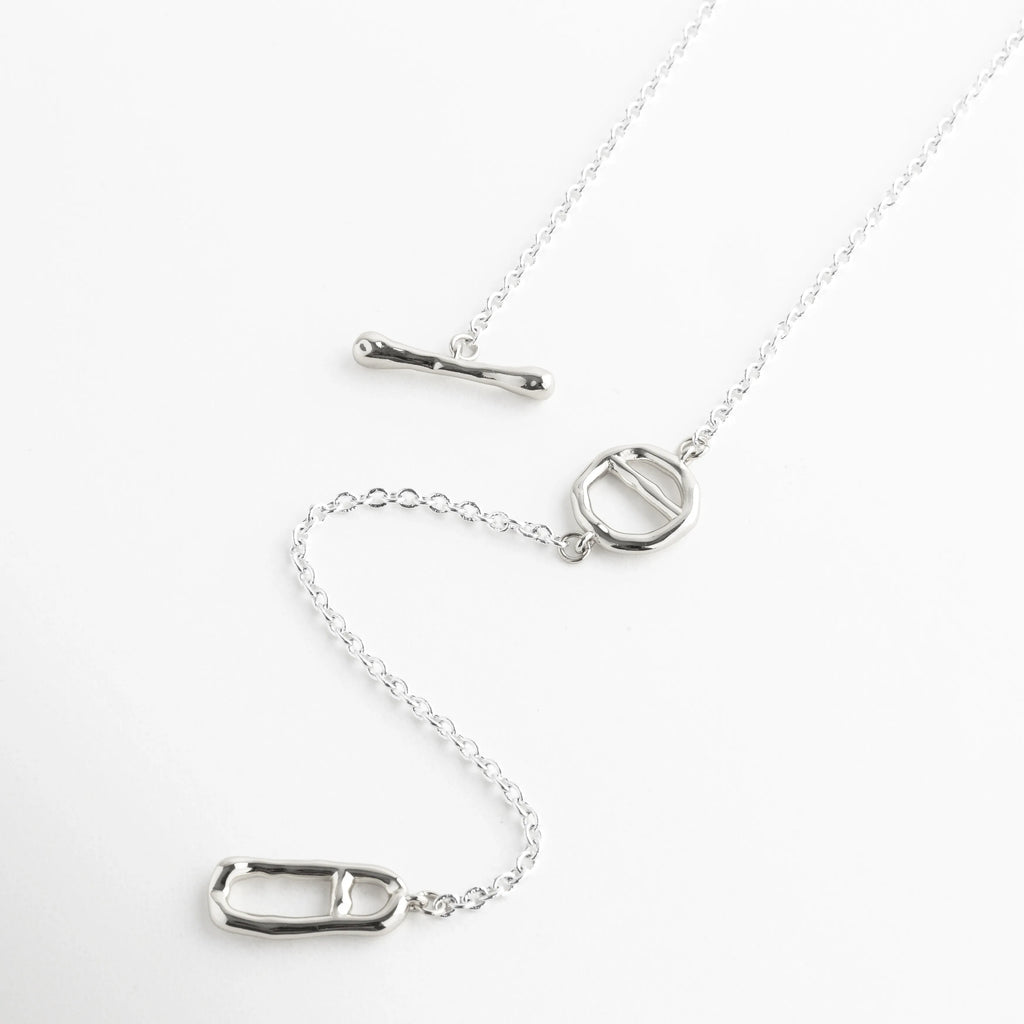 Collar lariat de oro blanco 18K con cierre de barra y colgante ovalado moderno, Gargantilla de plata 37 cm con diseño de cadena caída y elementos geométricos, Collar minimalista enchapado en oro blanco con dije ovalado y cierre T-bar, Joyas de acabado platinado con diseño asimétrico y eslabones finos de cobre, Vista completa de collar de oro blanco 18K con detalles de herrajes orgánicos.