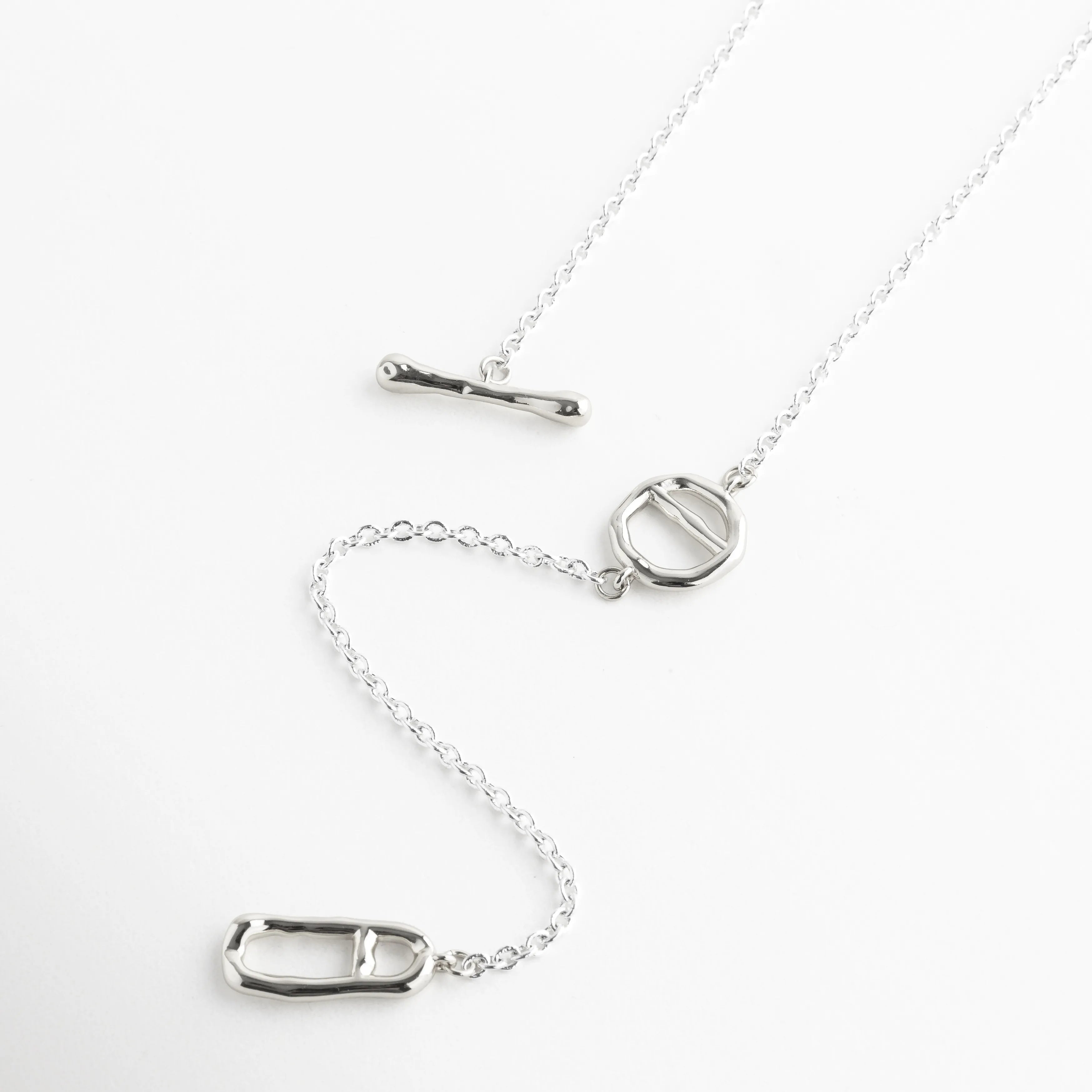 Collar lariat de oro blanco 18K con cierre de barra y colgante ovalado moderno, Gargantilla de plata 37 cm con diseño de cadena caída y elementos geométricos, Collar minimalista enchapado en oro blanco con dije ovalado y cierre T-bar, Joyas de acabado platinado con diseño asimétrico y eslabones finos de cobre, Vista completa de collar de oro blanco 18K con detalles de herrajes orgánicos.