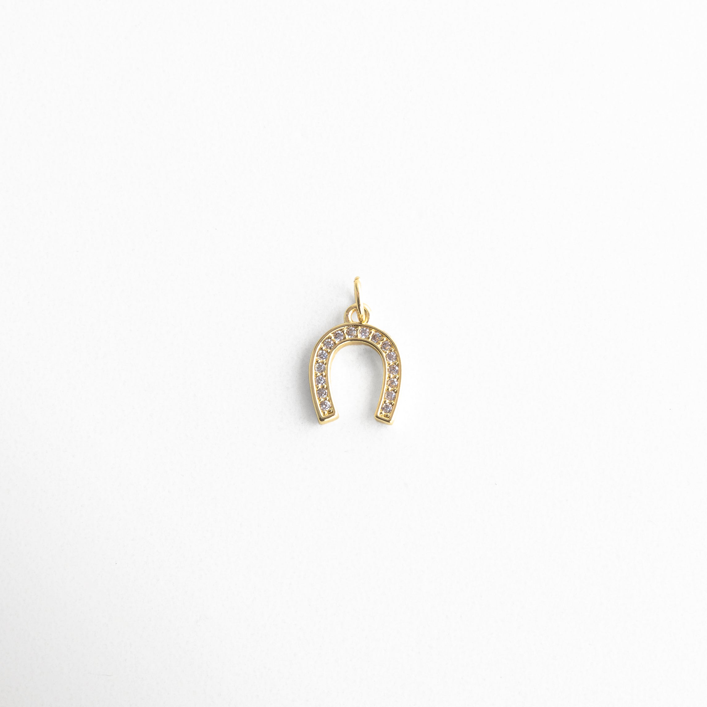 Charm dorado en forma de herradura con incrustaciones de zirconias, diseño brillante y elegante, símbolo clásico de buena suerte y protección, ideal para atraer energía positiva con un toque sofisticado