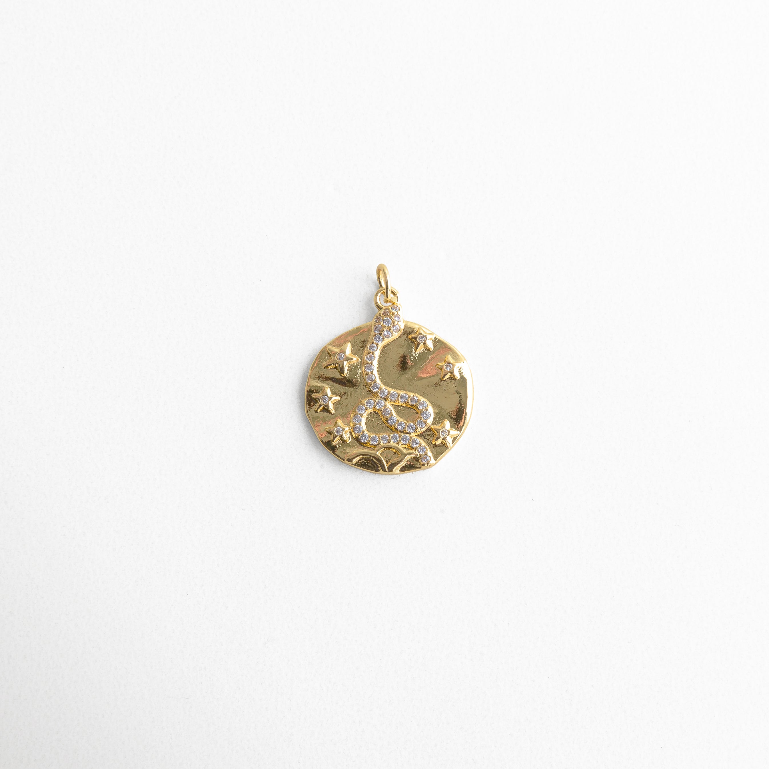 Charm dorado circular con diseño de serpiente decorada con zirconias y pequeñas estrellas en relieve, símbolo de transformación y poder, ideal para quienes buscan un accesorio con energía mística y elegante