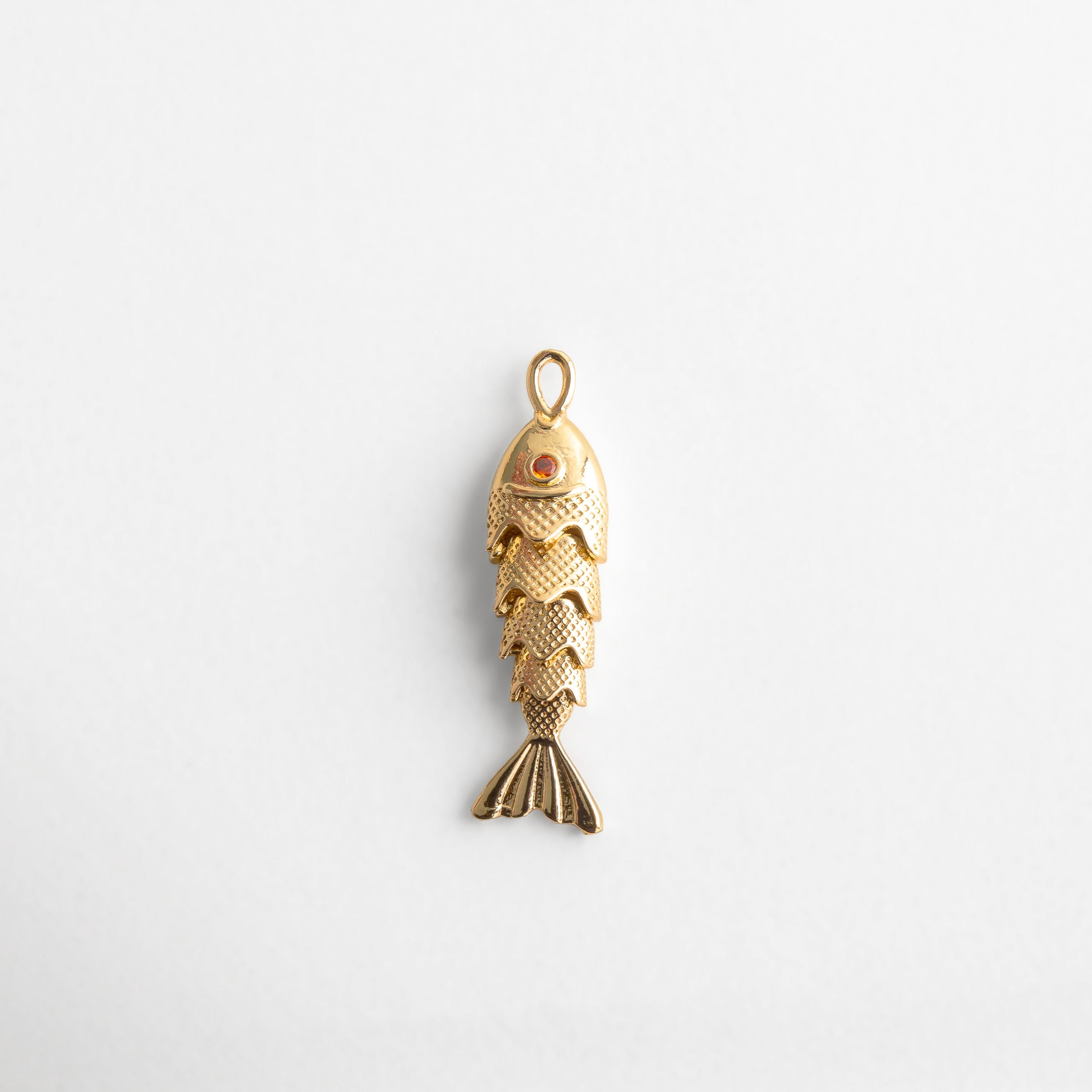 Charm dorado en forma de pez articulado con textura detallada y ojo con toque de color, diseño divertido y elegante que simboliza abundancia y buena fortuna, ideal para agregar movimiento y estilo a cualquier look