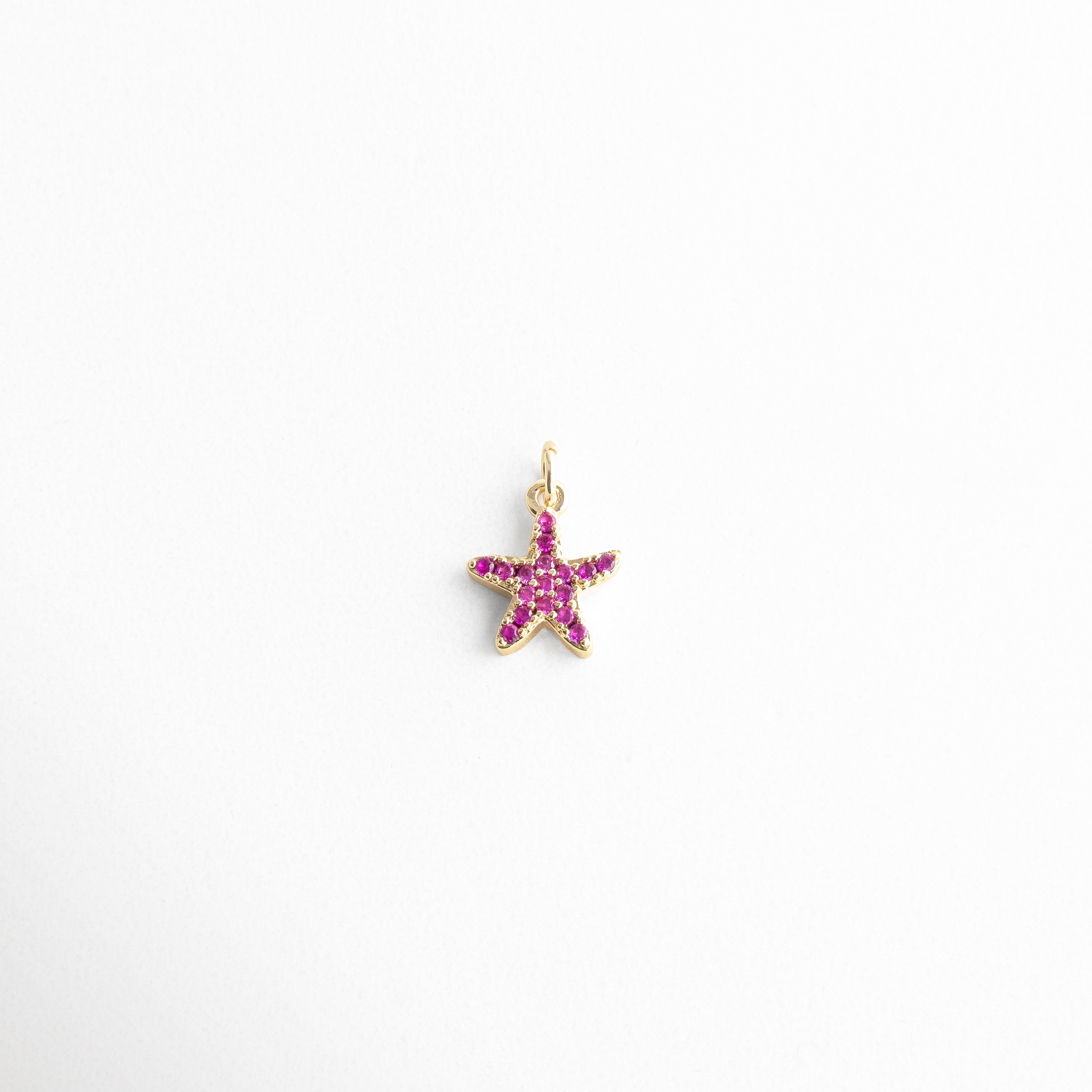 Charm dorado en forma de estrella de mar con incrustaciones de zirconias rosas, diseño delicado y veraniego, ideal para quienes aman el mar y buscan un toque de color y brillo en su look