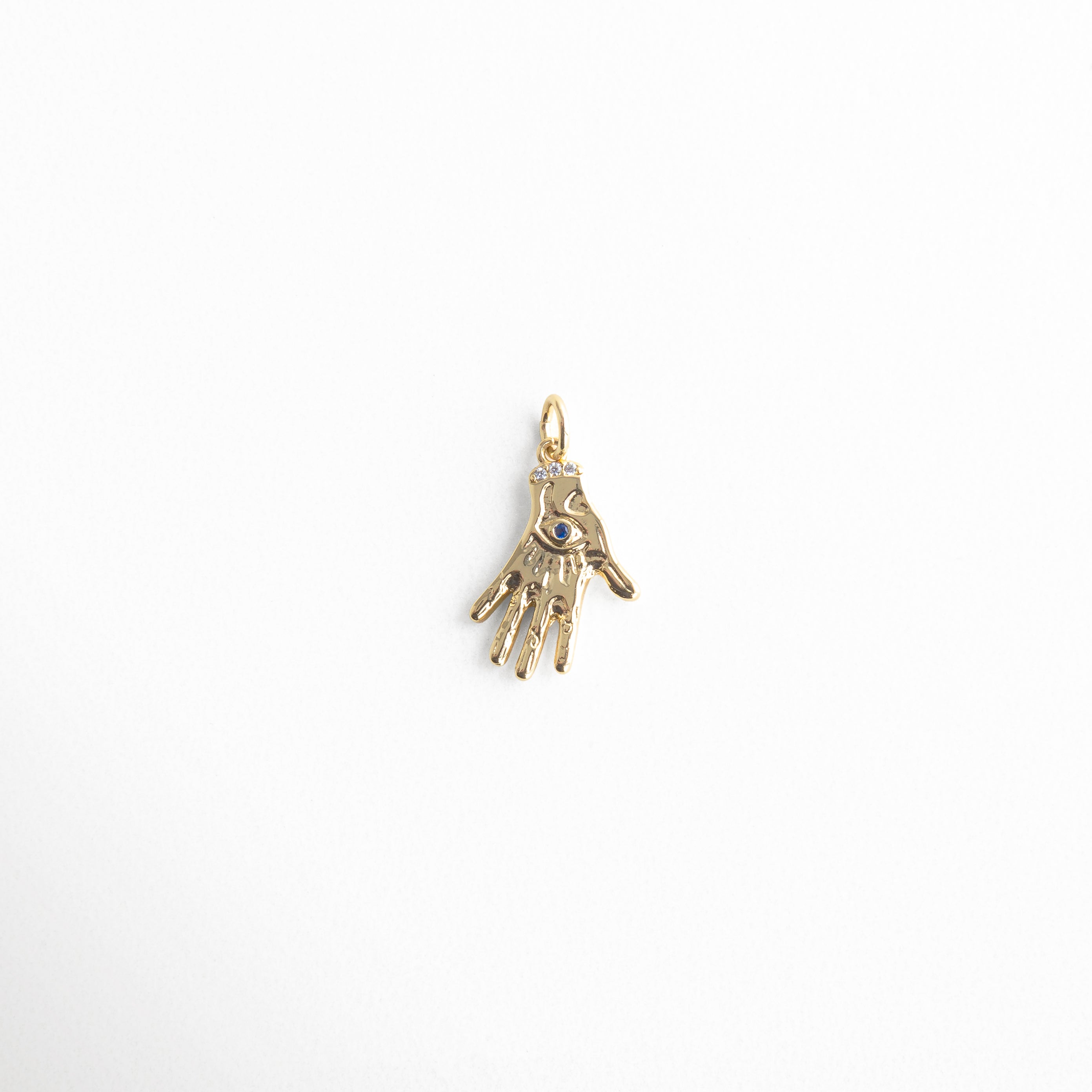 Charm dorado en forma de mano con detalle de ojo en el centro, símbolo de protección y energía espiritual, diseño delicado con incrustaciones brillantes, ideal para atraer buenas vibras y alejar las malas energías