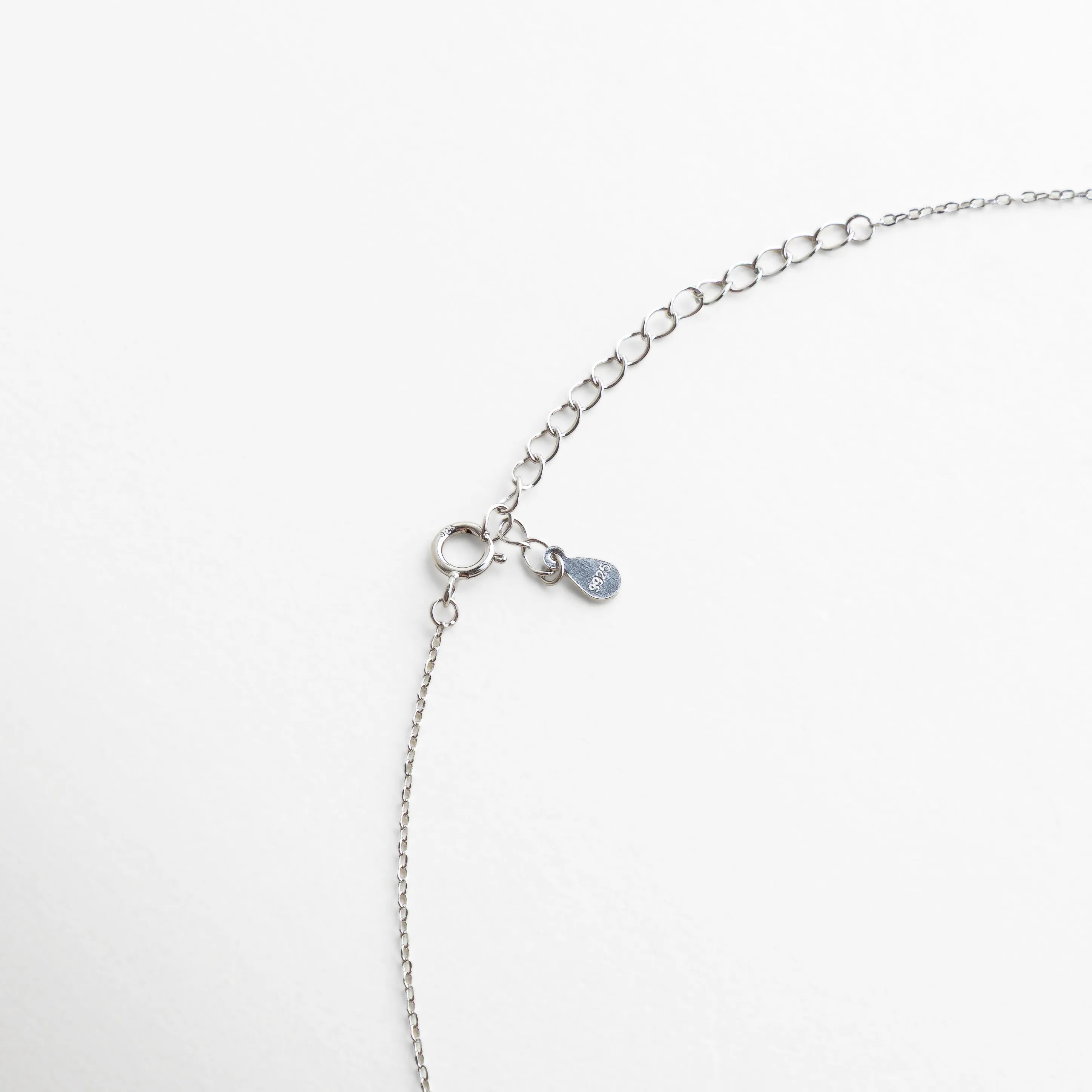 Cierre ajustable con extensión plateada y detalle de gota metálica grabada, acabado pulido y minimalista.