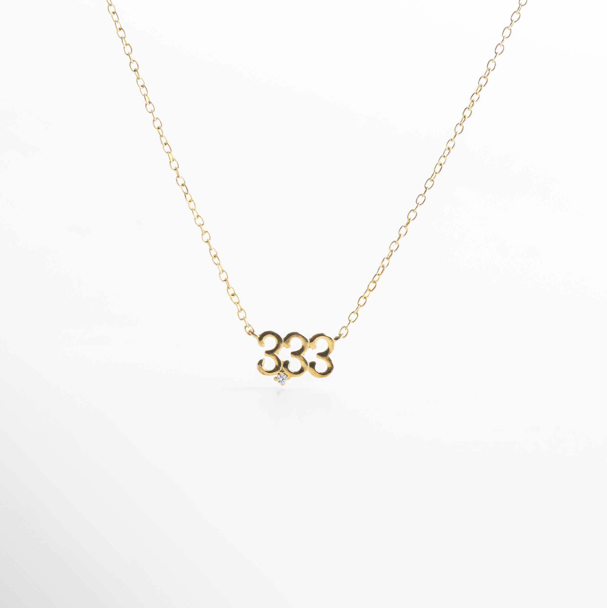 detalle del dije dorado número 333 con incrustaciones de zirconia, primer plano del número 333 en collar con acabado brillante, dije número 333 con zirconias montado en base de Plata .925, textura y brillo del número 333 en diseño cuadrado, zirconias incrustadas en dije dorado número 333