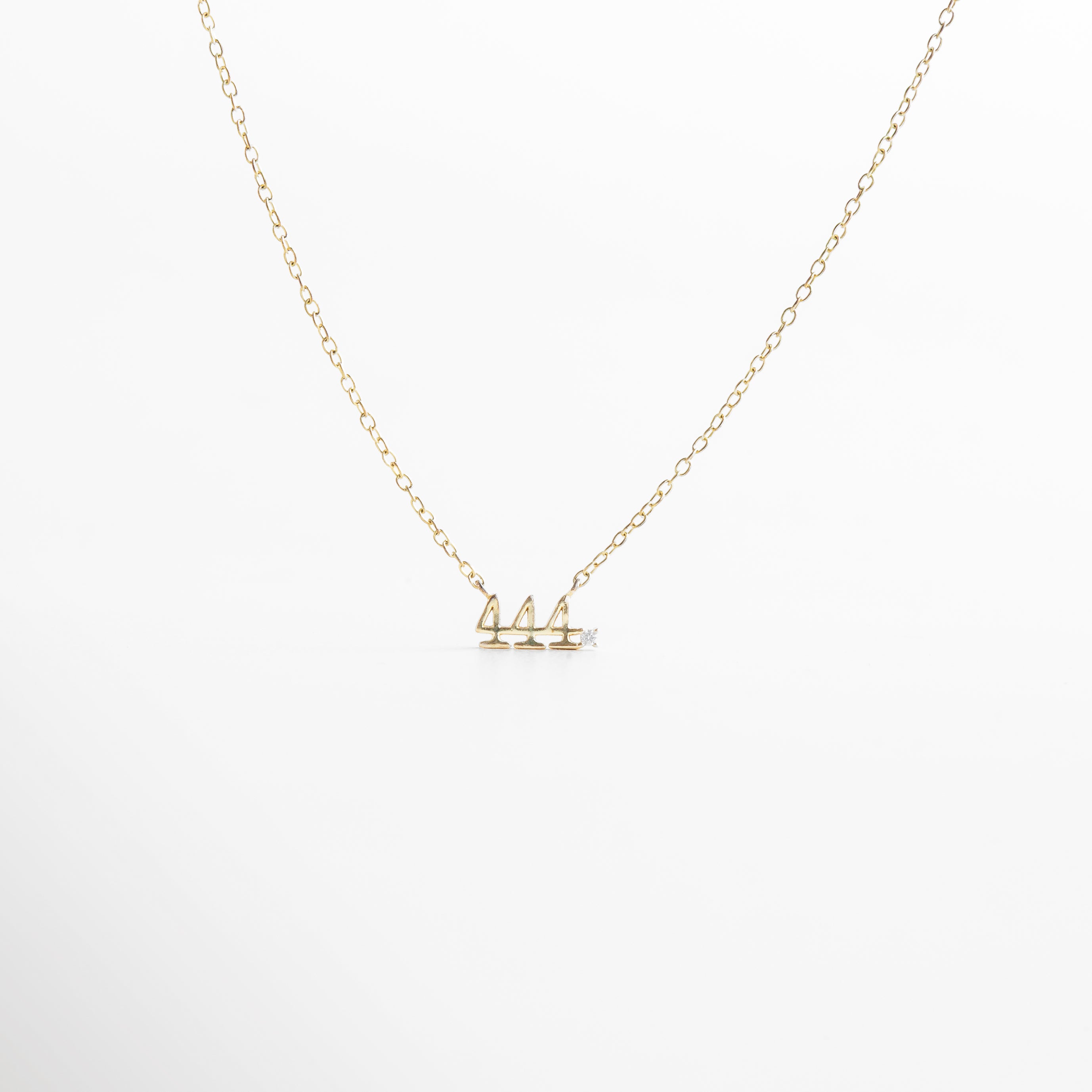 reflejo de luz sobre zirconias del número 444, brillo delicado del dije número 444 en acabado dorado, textura del collar 444 en plano cerrado, brillo espiritual del collar con número angelical, destello sutil en zirconias sobre el número 444