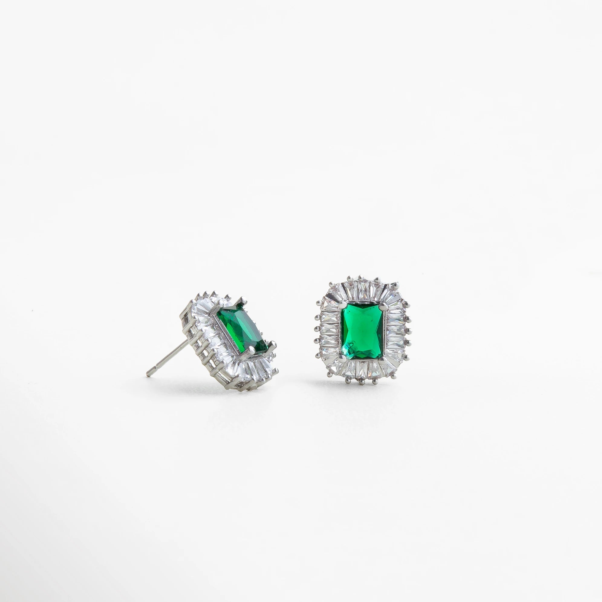 Vista lateral de aretes plateados con piedra verde tipo esmeralda, detalle del engaste y acabado pulido que realza el brillo y la profundidad del color.