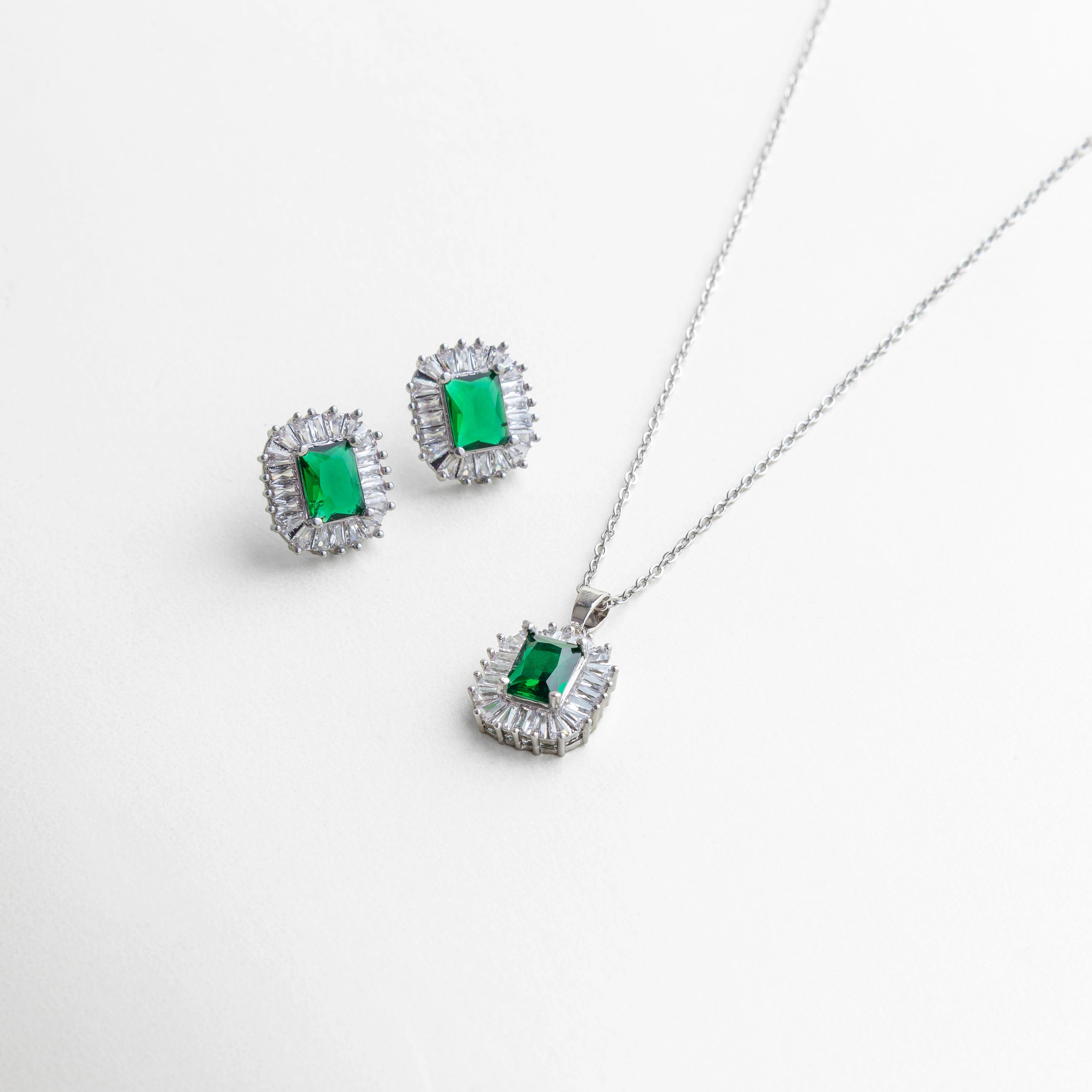 Set de joyería plateado con collar y aretes a juego, piedra verde rectangular tipo esmeralda rodeada de halo brillante, diseño elegante y sofisticado.