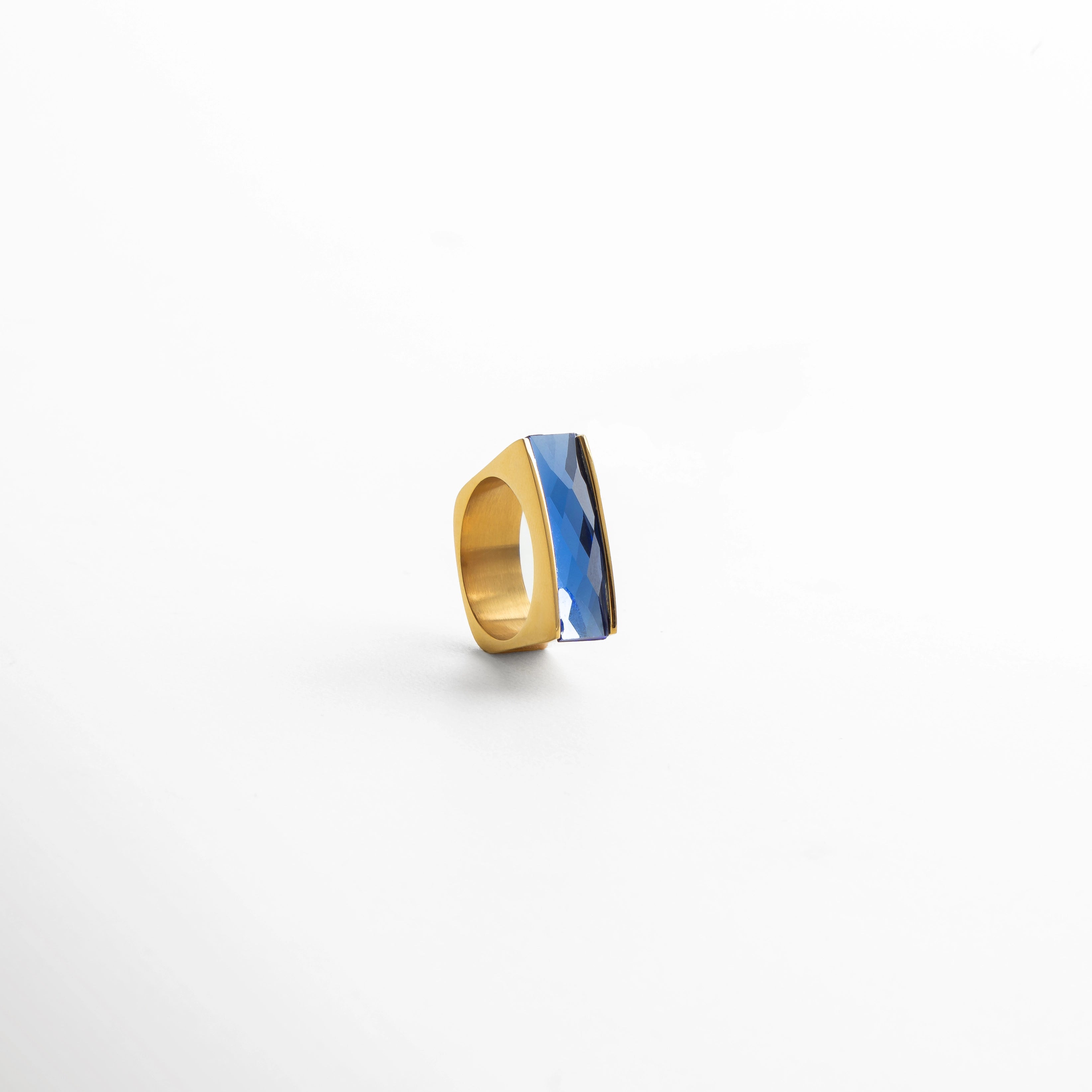 Anillo dorado con piedra azul rectangular, joya de diseño vanguardista con acabado pulido y detalles angulares.