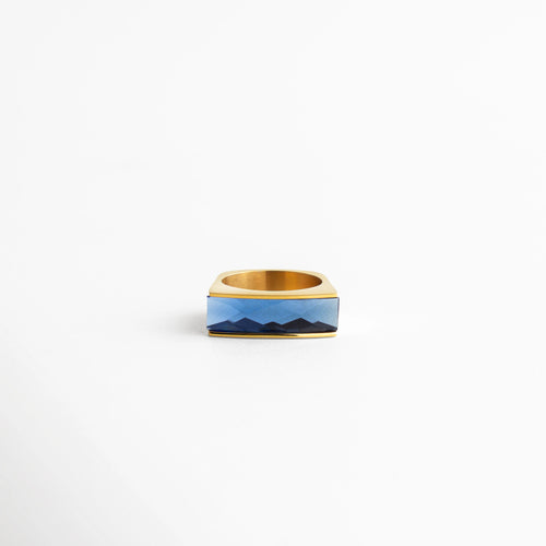 Anillo dorado con piedra azul rectangular facetada, diseño elegante con brillo intenso, ideal para destacar cualquier outfit.