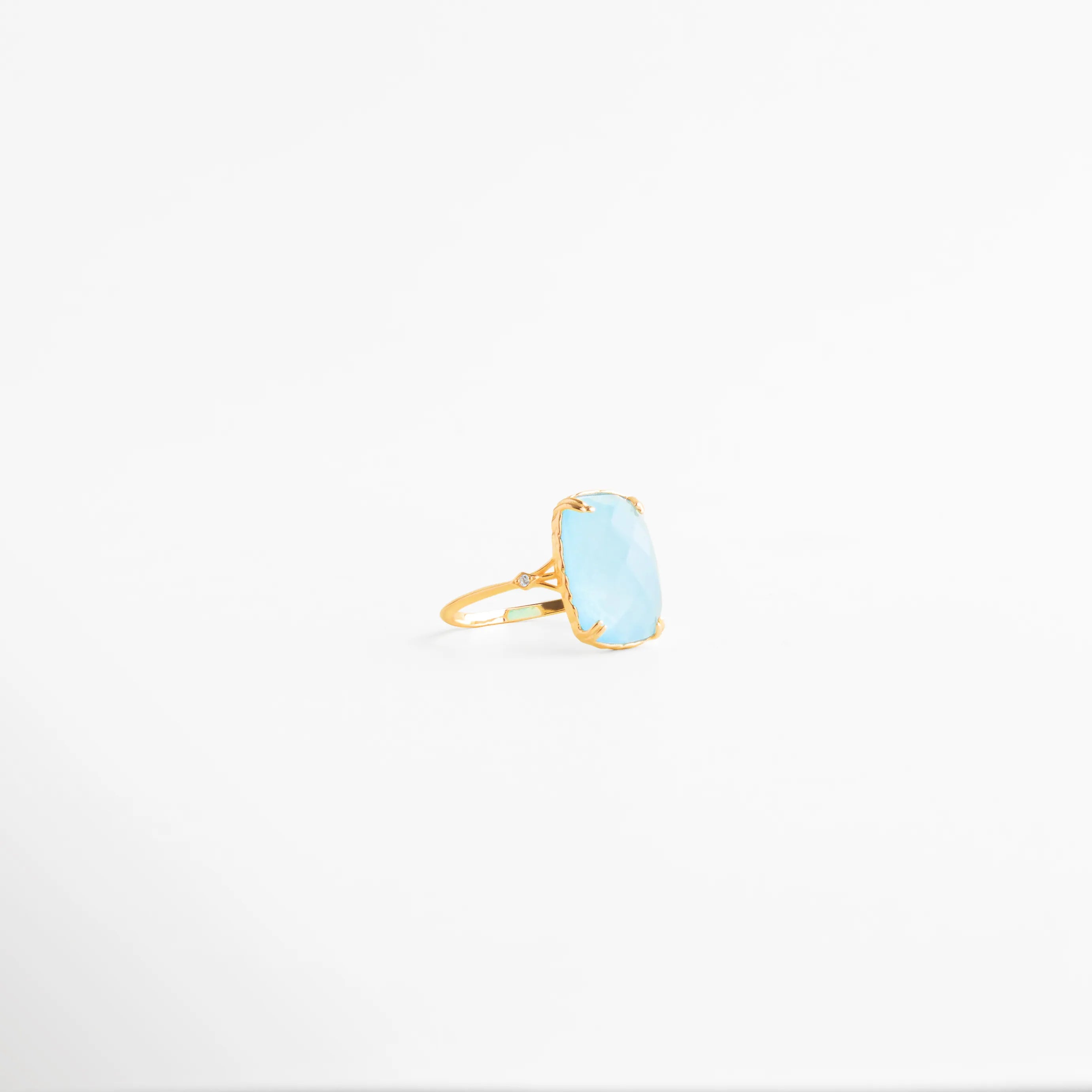 anillo dorado vista lateral con piedra azul clara, perfil de anillo delicado con piedra azul, anillo fino dorado con engaste elevado azul, detalle lateral de anillo elegante azul, anillo femenino vista costado joyería