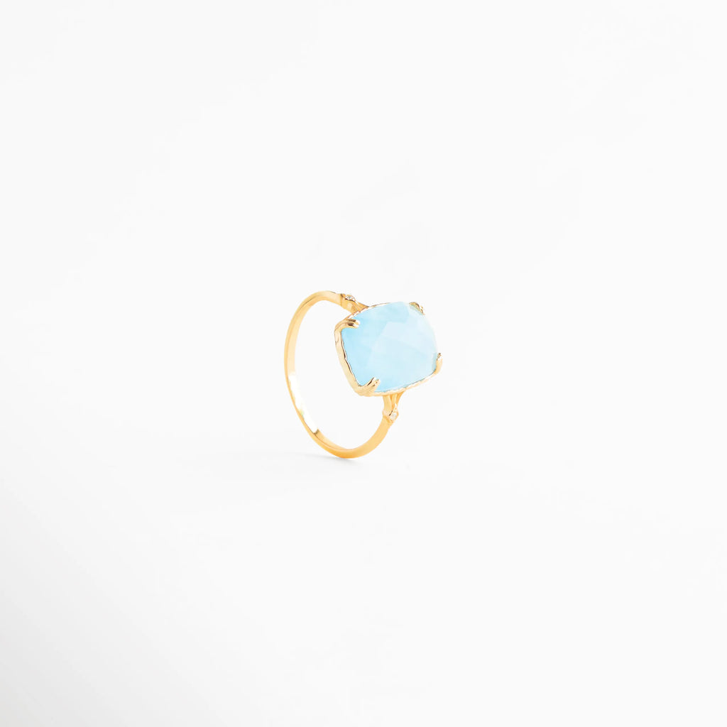 anillo dorado con piedra azul vista tres cuartos, anillo elegante con piedra azul clara en ángulo, joyería fina anillo azul estilo moderno, anillo delicado dorado con piedra azul clara, anillo sofisticado con piedra azul vista diagonal