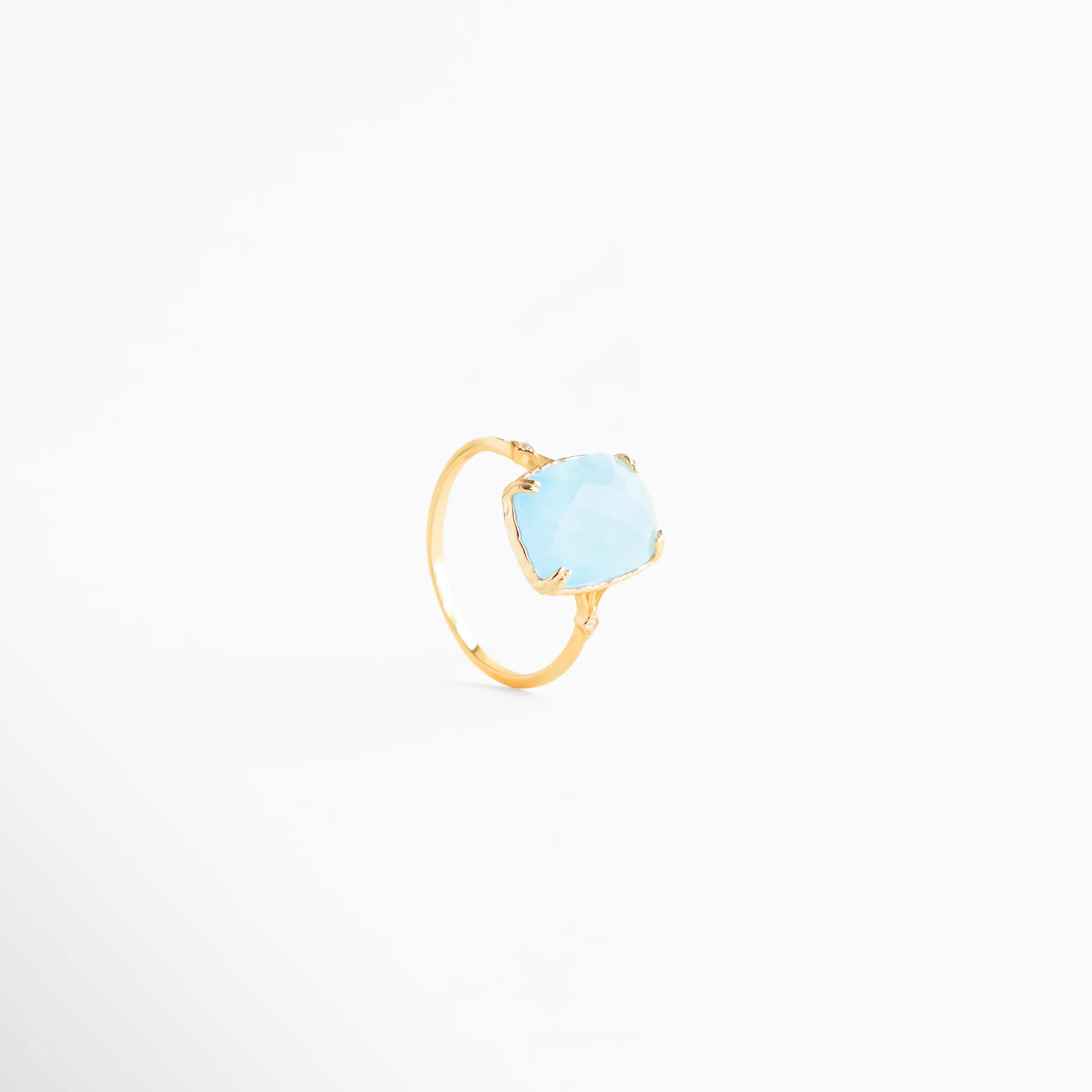 anillo dorado con piedra azul vista tres cuartos, anillo elegante con piedra azul clara en ángulo, joyería fina anillo azul estilo moderno, anillo delicado dorado con piedra azul clara, anillo sofisticado con piedra azul vista diagonal