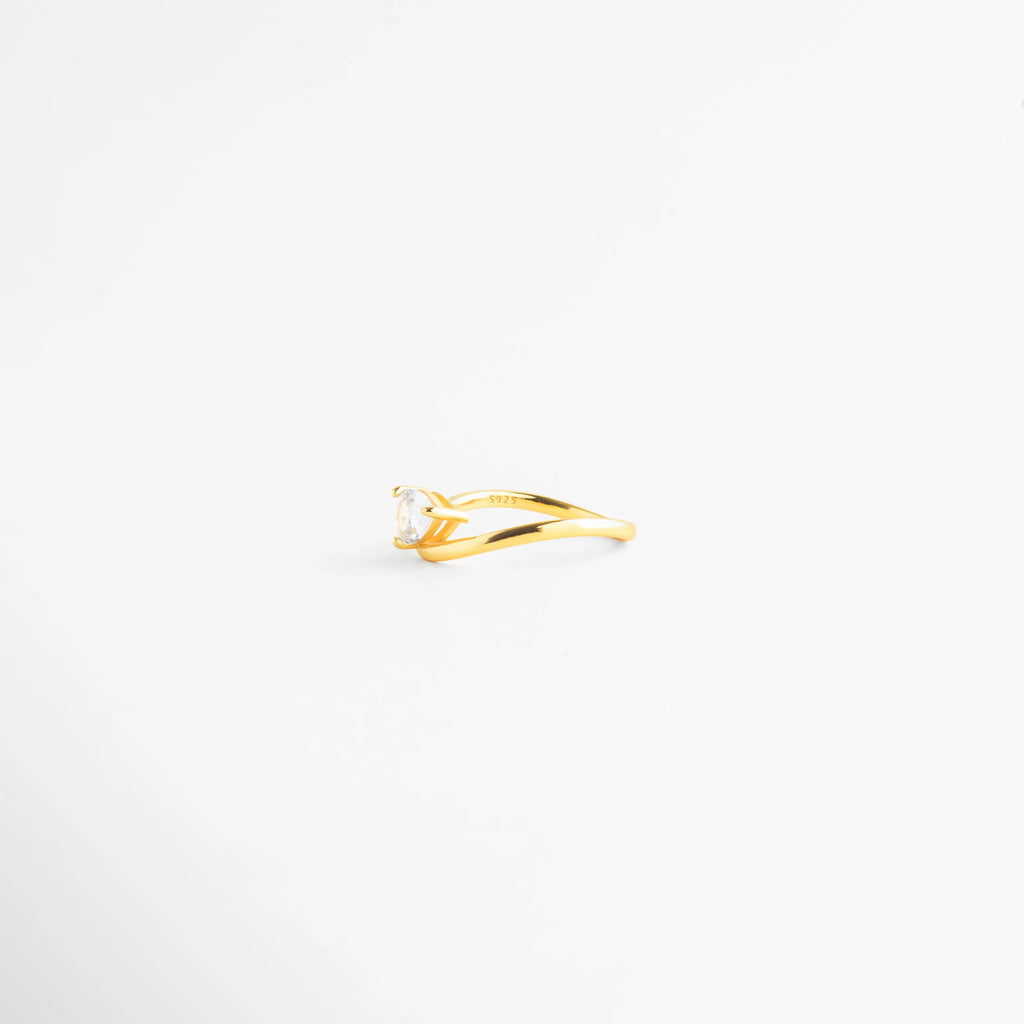 Vista de perfil plano de anillo de plata mostrando la curvatura de la banda, Detalle del grosor de 0.4 cm de la banda del anillo de plata dorada, Anillo solitario moderno con zirconia engastada sobre banda curva, Silueta lateral de anillo de plata ley 925 con baño de oro, Estructura ergonómica de anillo minimalista con piedra central.