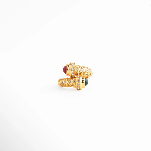 anillo dorado con diseño envolvente y piedra roja, anillo statement dorado con detalle brillante, anillo elegante con acento rojo central, joyería dorada sofisticada estilo moderno, anillo llamativo de acabado pulido, anillo dorado con diseño artístico