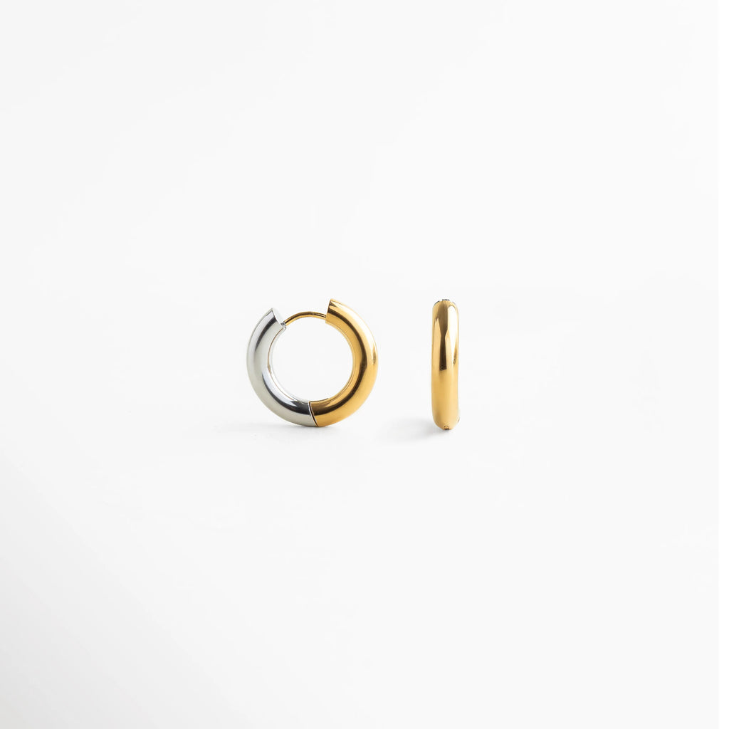Aretes de argolla bitono en acero inoxidable con mitad dorada y mitad plateada, Arracadas pequeñas de acero inoxidable con diseño dividido en color oro y plata, Vista frontal de aretes "huggie" bitono con acabado pulido y brillante, Joyería versátil: aretes de acero inoxidable que combinan tonos dorados y plateados, Detalle de argollas modernas de acero con transición de color bitono.