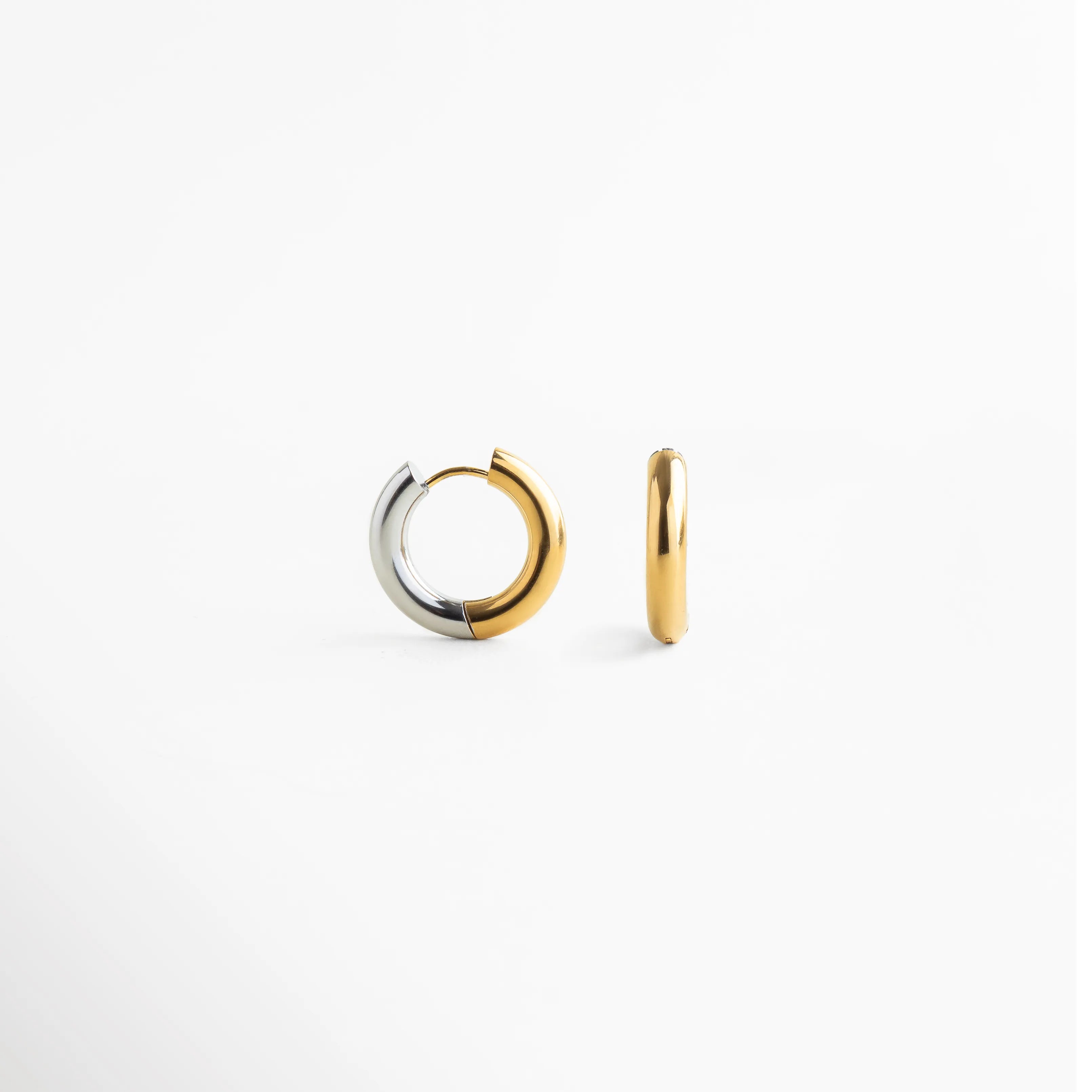 Aretes de argolla bitono en acero inoxidable con mitad dorada y mitad plateada, Arracadas pequeñas de acero inoxidable con diseño dividido en color oro y plata, Vista frontal de aretes "huggie" bitono con acabado pulido y brillante, Joyería versátil: aretes de acero inoxidable que combinan tonos dorados y plateados, Detalle de argollas modernas de acero con transición de color bitono.