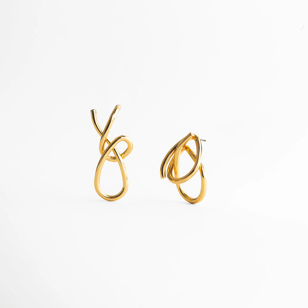 detalle de aretes dorados con formas fluidas, textura lisa y pulida en aretes dorados, diseño entrelazado en aretes de acabado brillante, joyería dorada con líneas suaves y orgánicas, aretes dorados con diseño artístico moderno, detalle cercano de aretes tipo nudo dorados