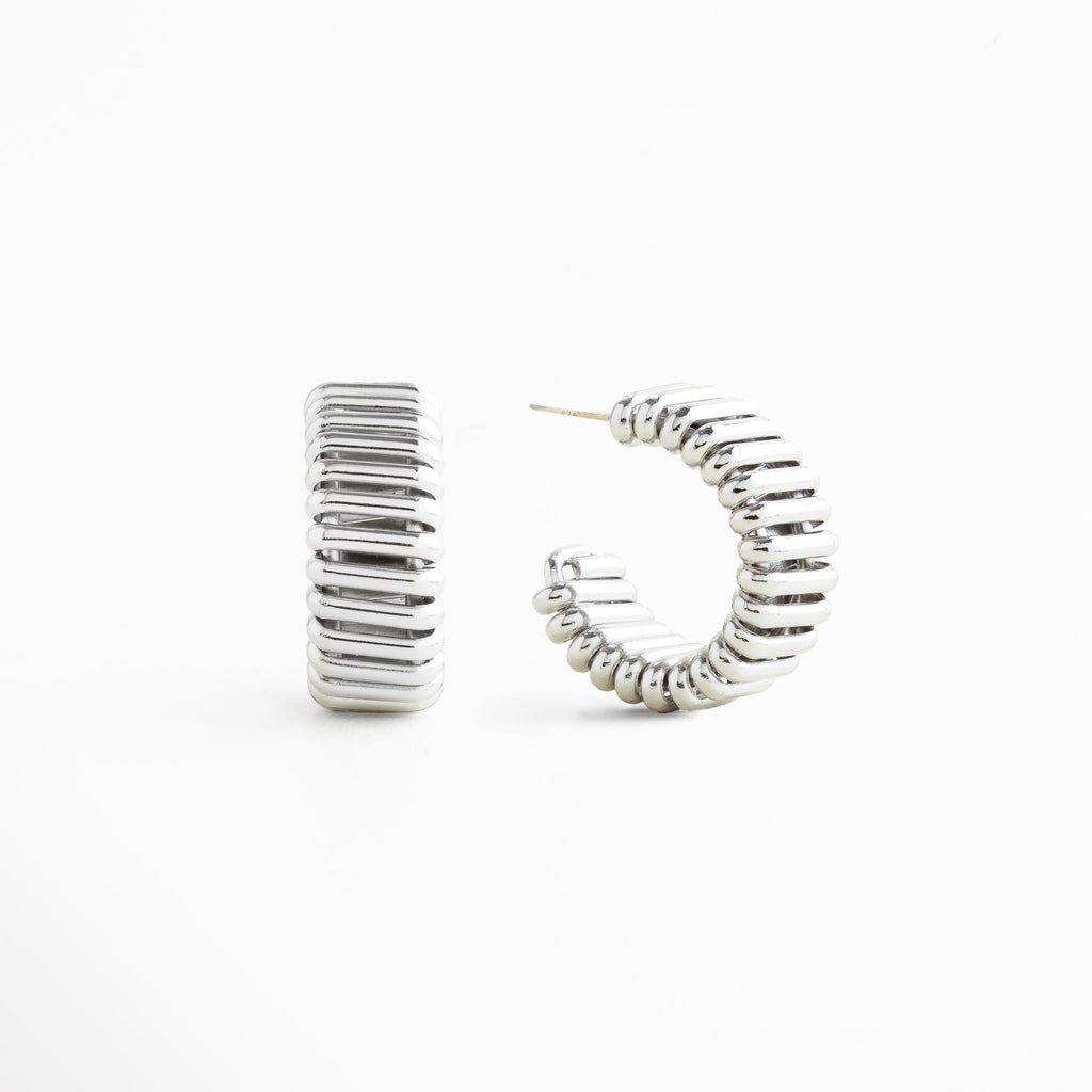 detalle de aretes hoops plateados acabado pulido, textura lisa en aretes chunky plateados, brillo metálico en aretes futuristas plateados, diseño voluminoso en aretes tipo aro plateados, acabado espejo en aretes statement