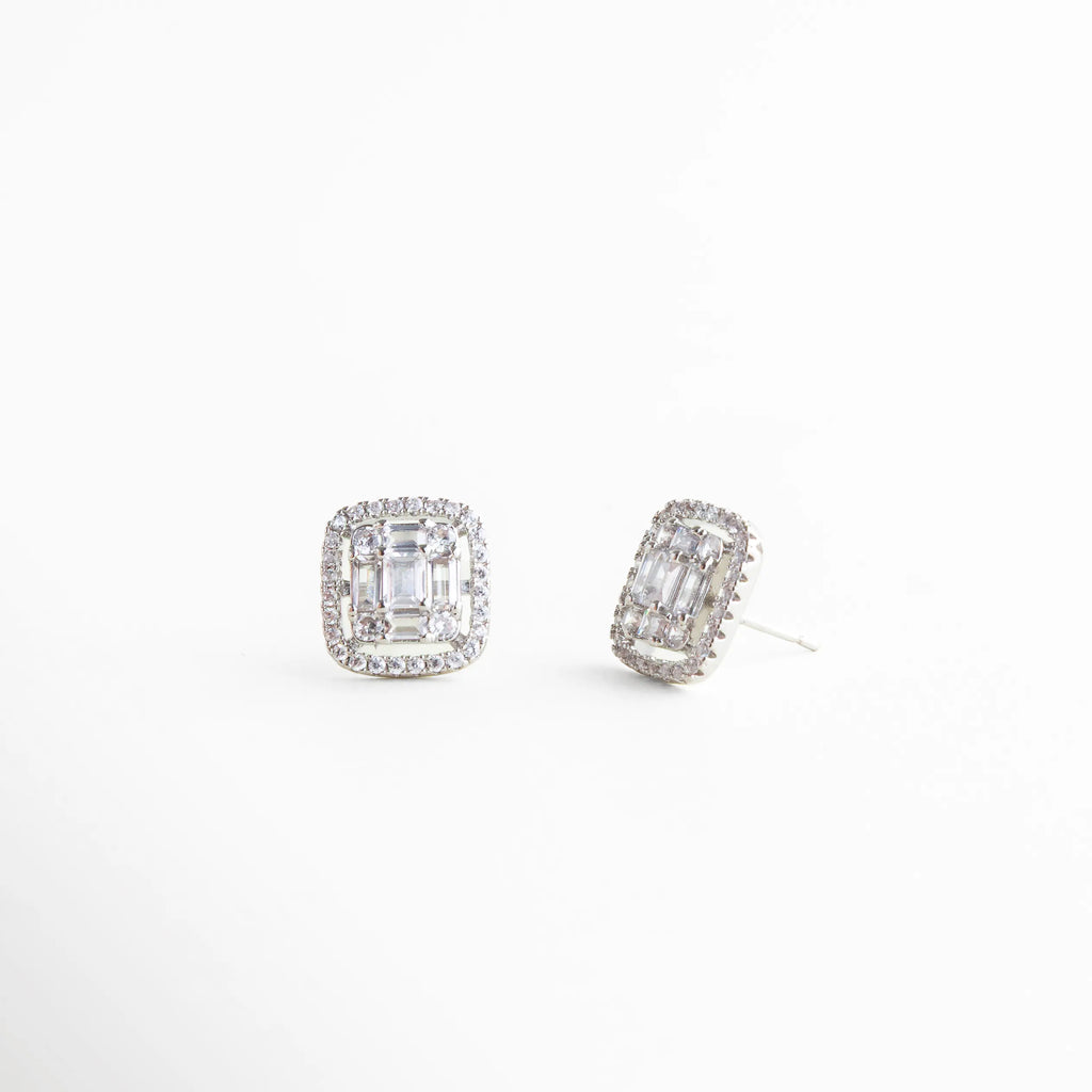 Detalle de aretes plateados con cristales claros y acabado pulido, Primer plano de aretes pequeños con brillo delicado y diseño fino, Aretes plateados con engaste de cristales en diseño elegante, Textura brillante en aretes delicados plateados, Aretes minimalistas con cristales claros y estilo refinado